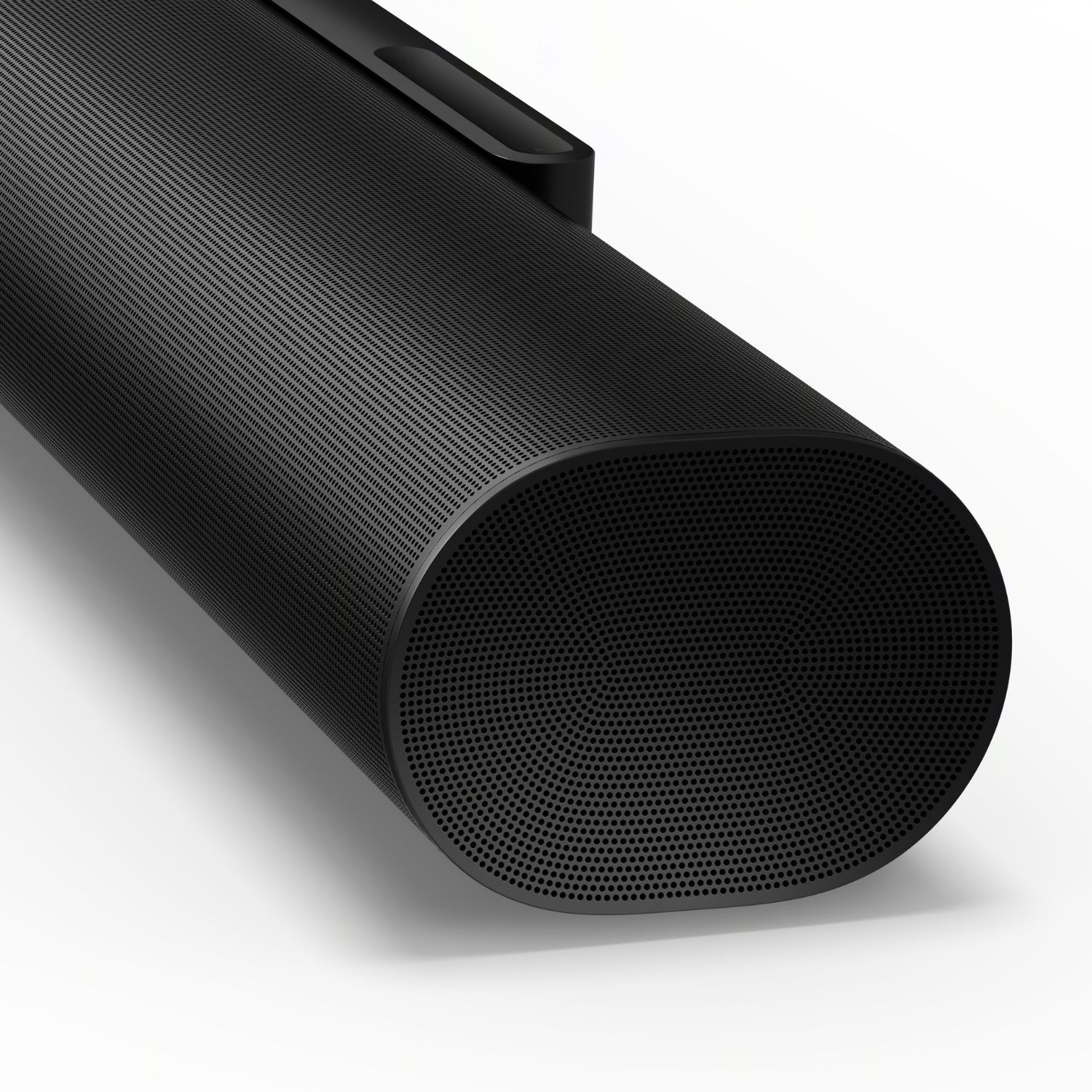 Una barra de sonido Sonos negra sobre una superficie blanca. El altavoz tiene forma curva y muchos agujeros.