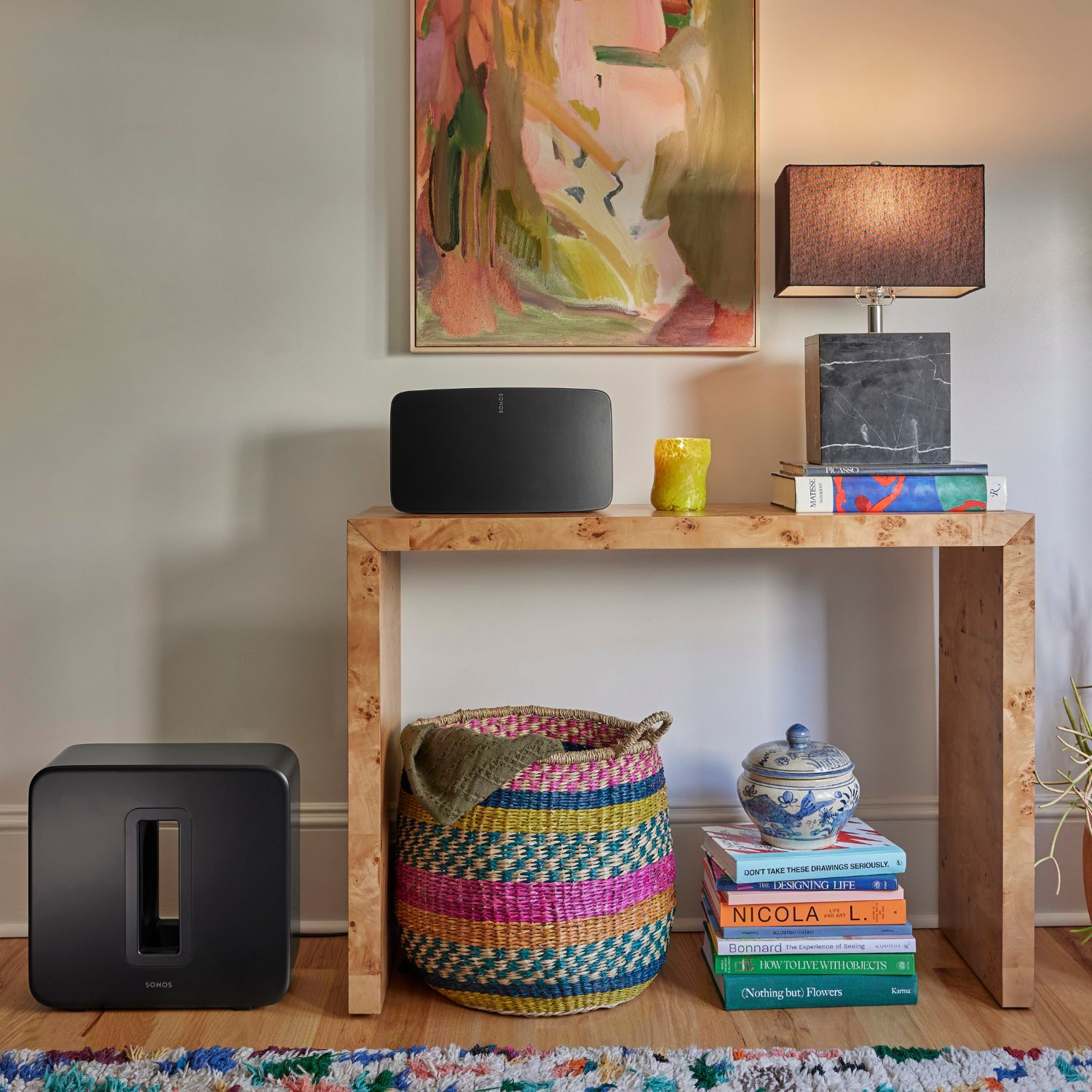 Salón con altavoz, subwoofer y libros en mesa de madera. Una alfombra colorida.