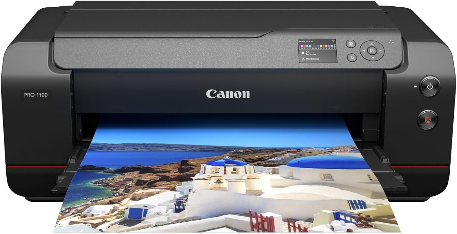 Una impresora negra Canon PRO-1100 está imprimiendo una imagen vibrante de un pueblo costero con edificios de cúpulas azules y mar azul.