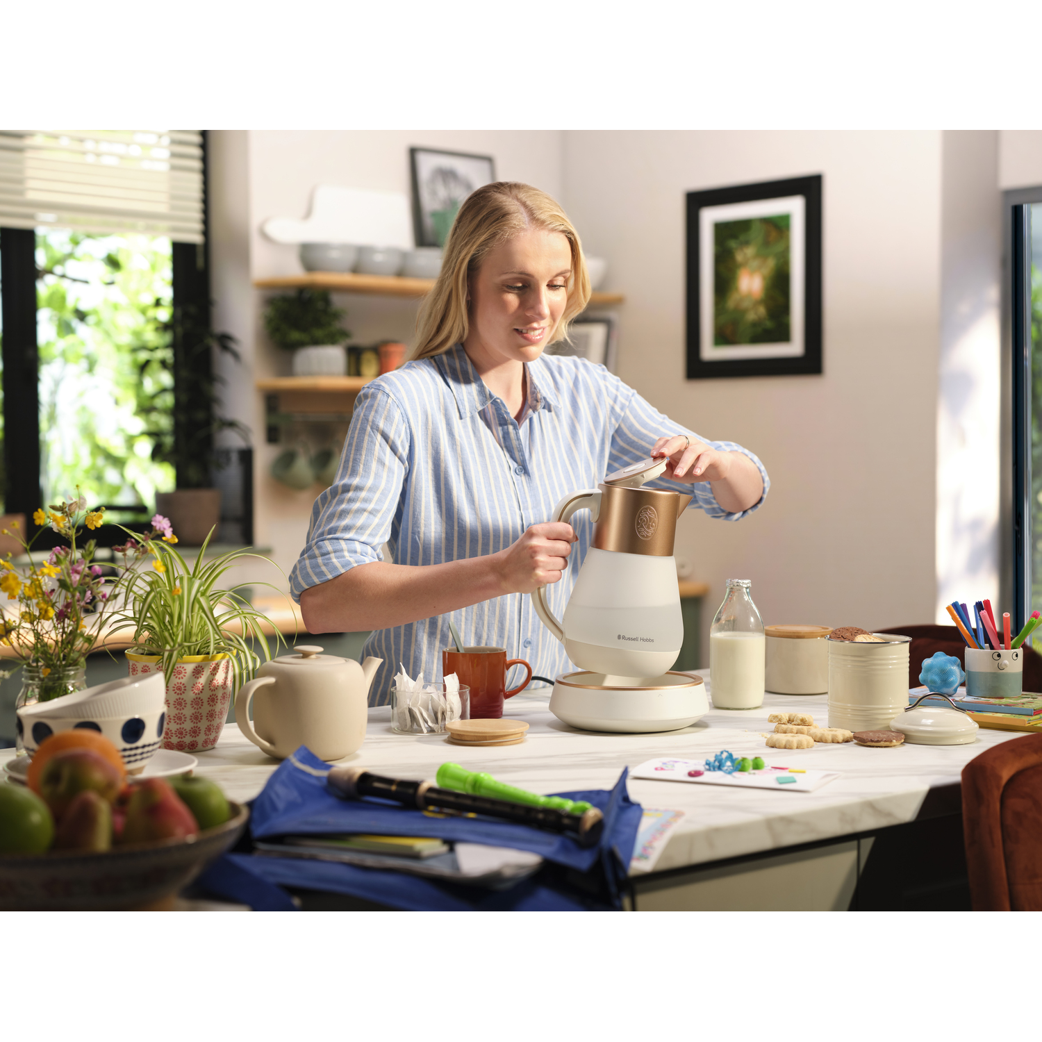 Woman in a kitchen using a kettle and preparing a drink. Various items on the table.