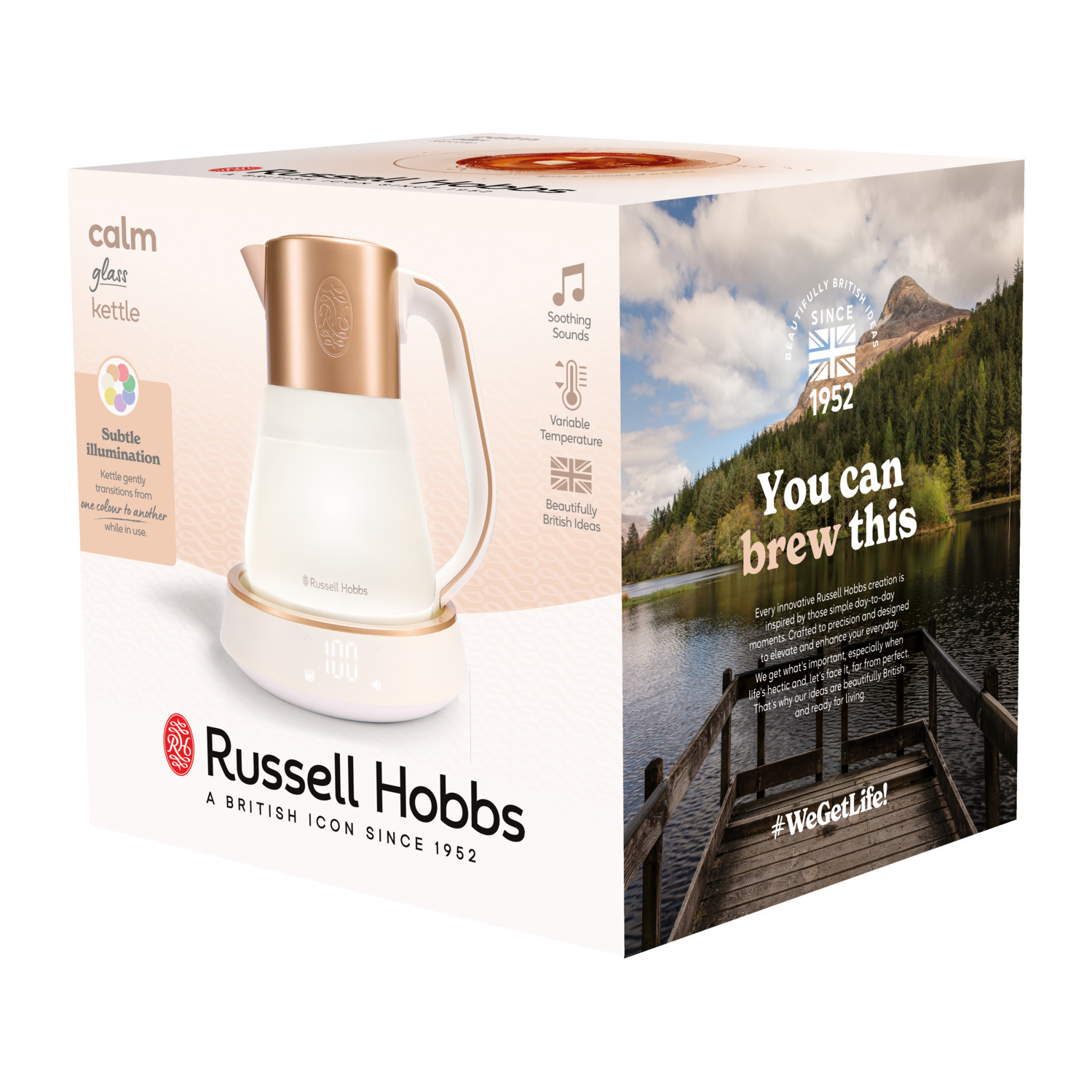 A kettle in a box with text about it. The kettle is white and gold. The background is a lake and mountains.