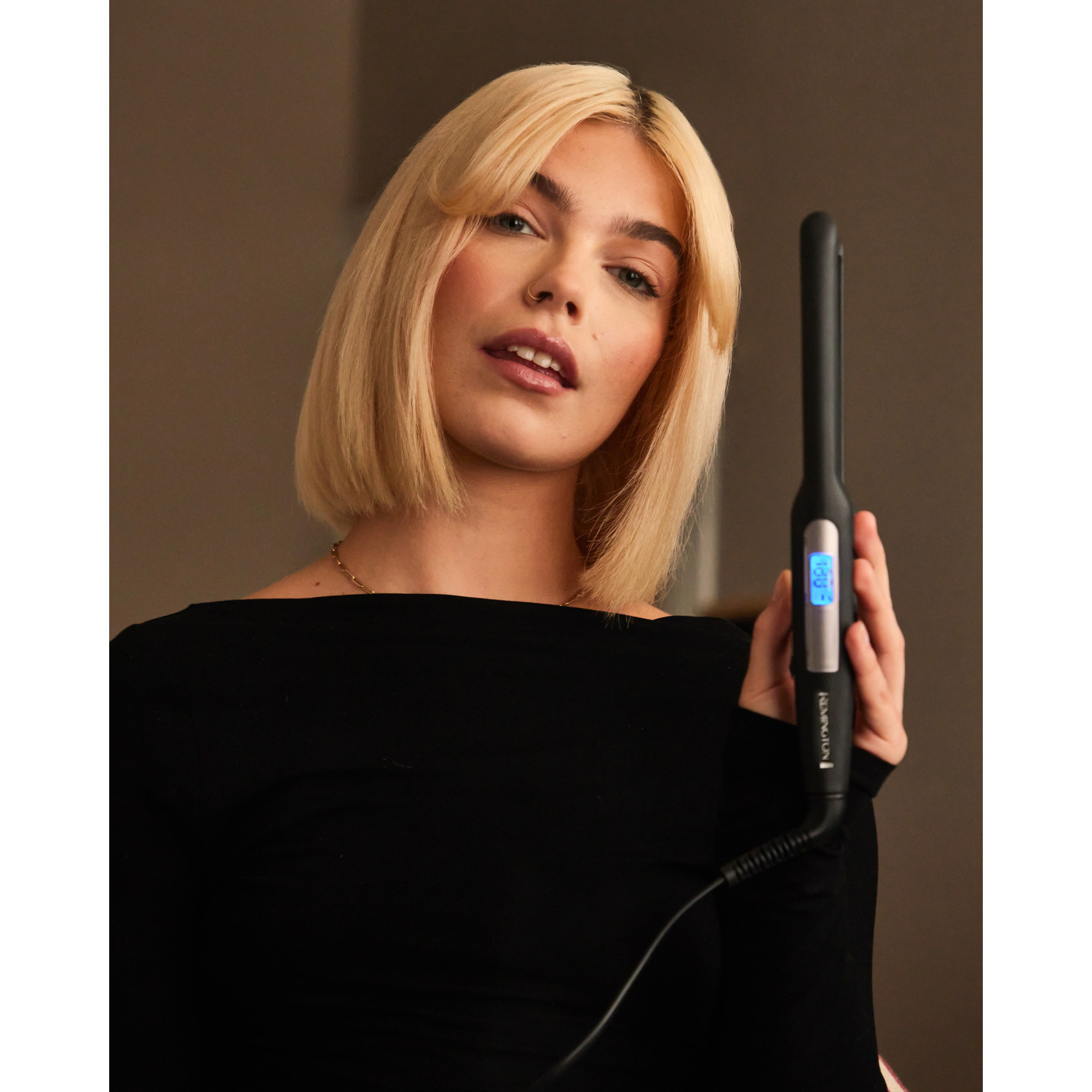 Une femme tient un lisseur noir. Elle est blonde et regarde vers la caméra.