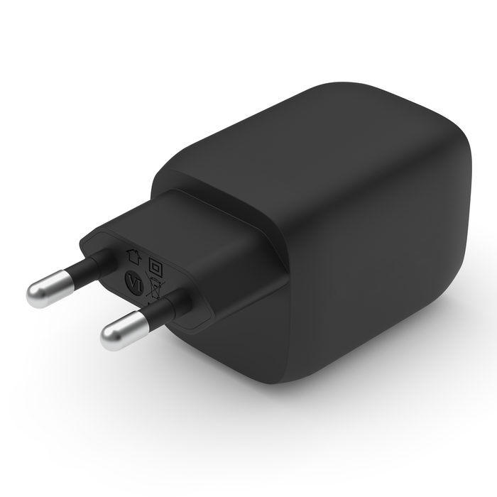 Un adaptador de corriente negro con clavijas plateadas sobre una superficie blanca.