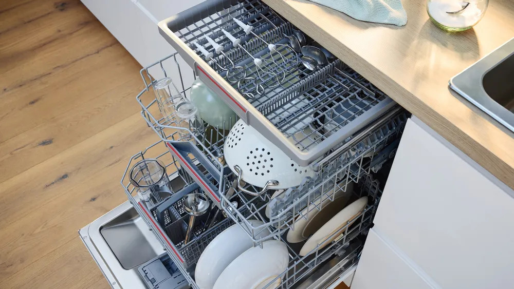 Zmywarka z naczyniami i sztućcami w środku, szuflady są otwarte.