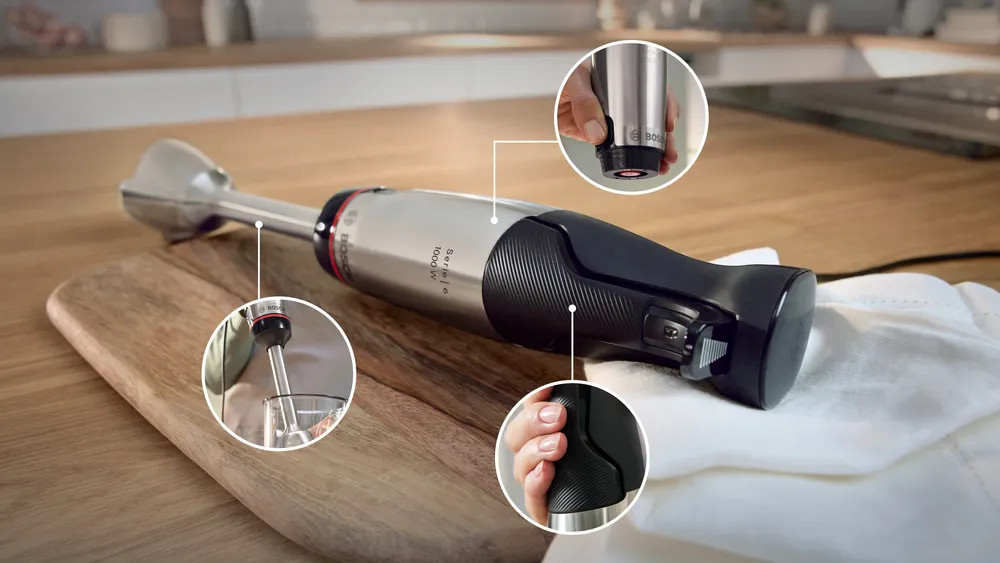 Srebrno-czarny blender ręczny z trzema zbliżeniami na drewnianej desce.