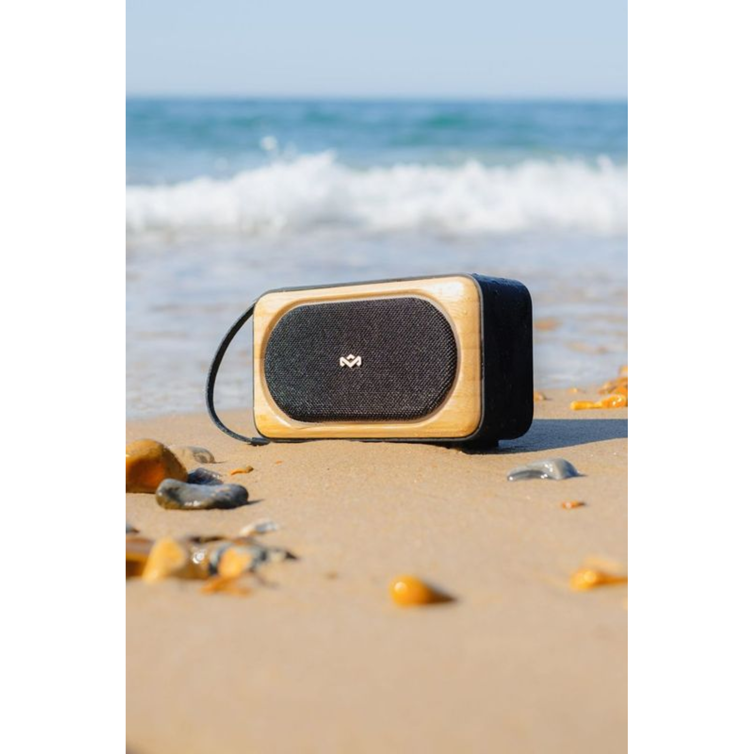 Portable speaker on a sandy beach with the ocean in the background. Wooden frame and black fabric.