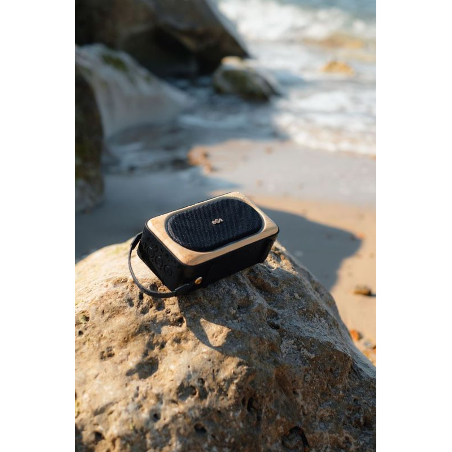 A black and wood-colored speaker on a rock at the beach.