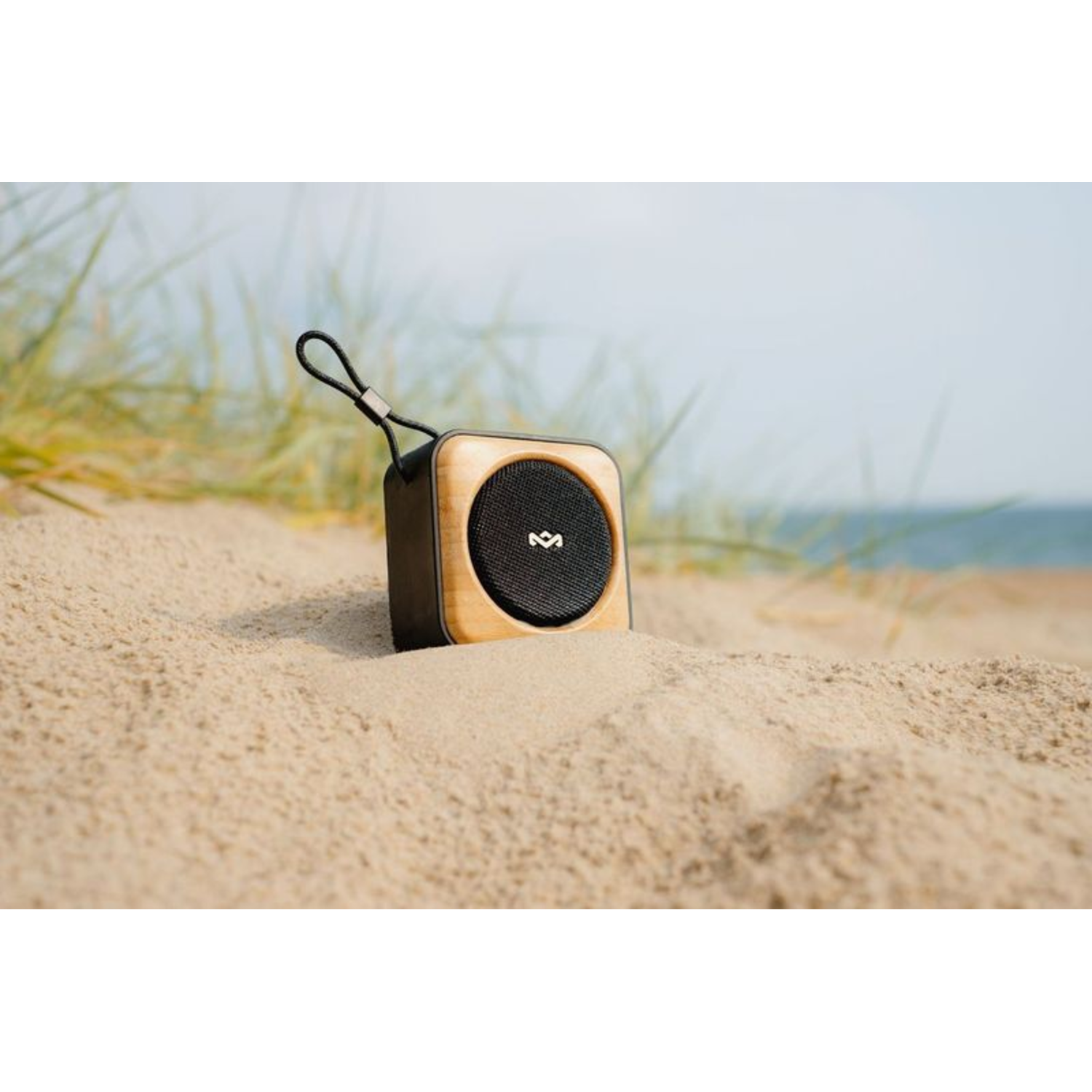 Small wooden speaker box with a black mesh speaker, on a sandy beach with sea.