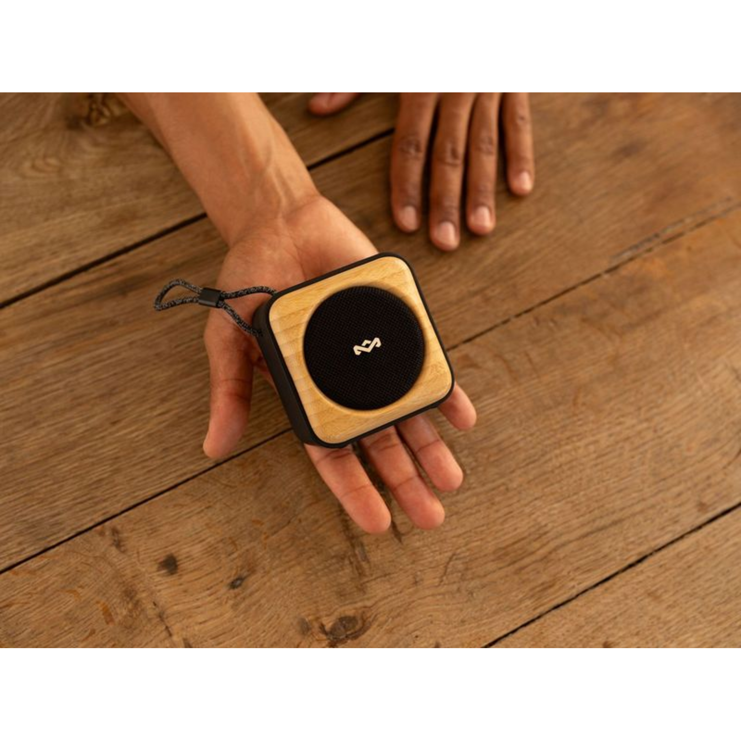 A small wooden speaker on a hand, on a wooden table. The speaker is black.