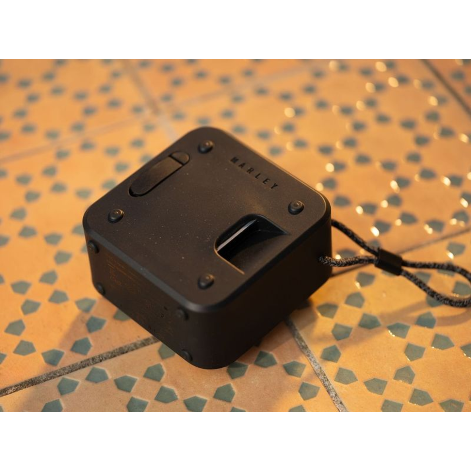 A black, square speaker with the brand name MARLEY on the top. It's on a tiled surface.