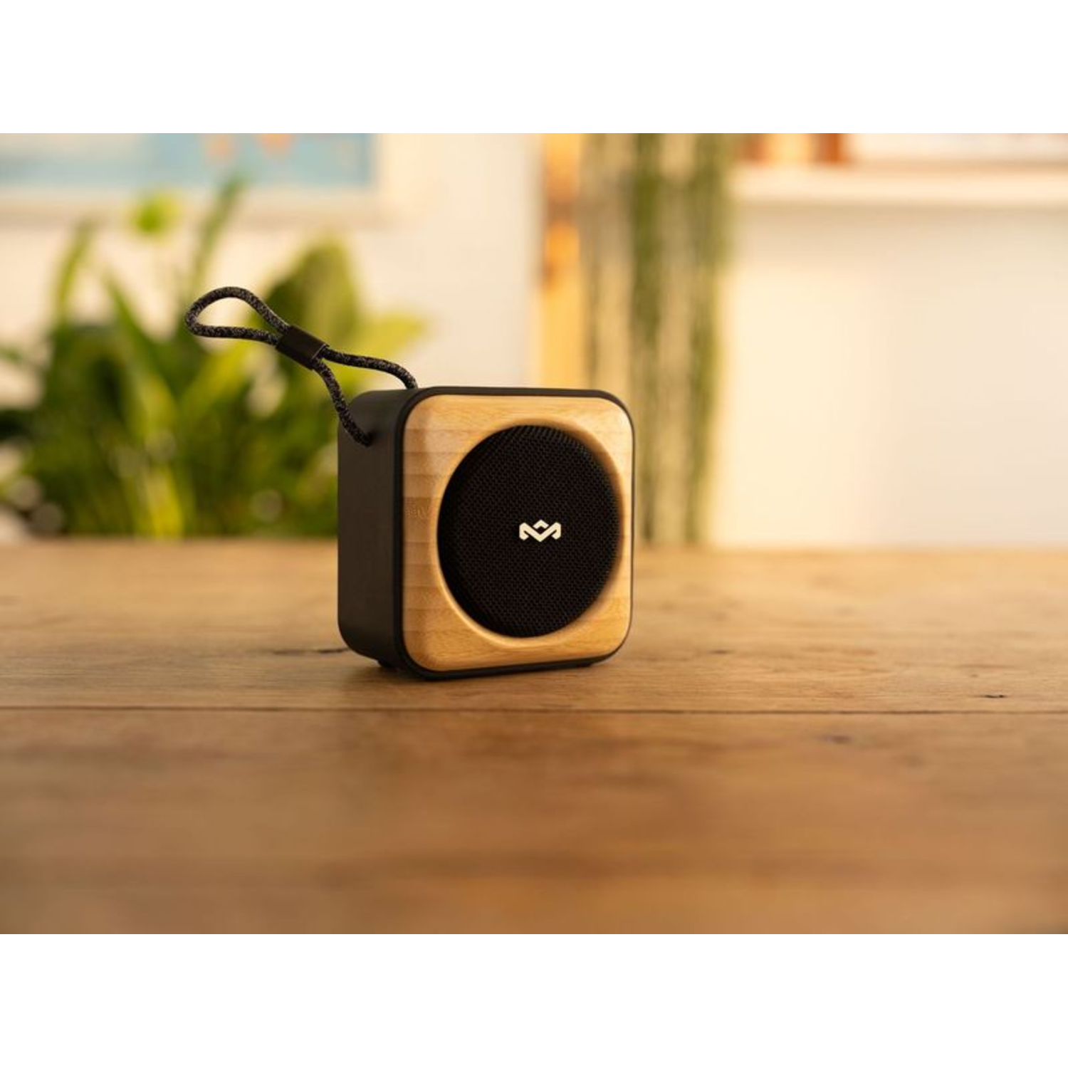 A small, black and wood speaker on a wooden table. A black cord is attached.