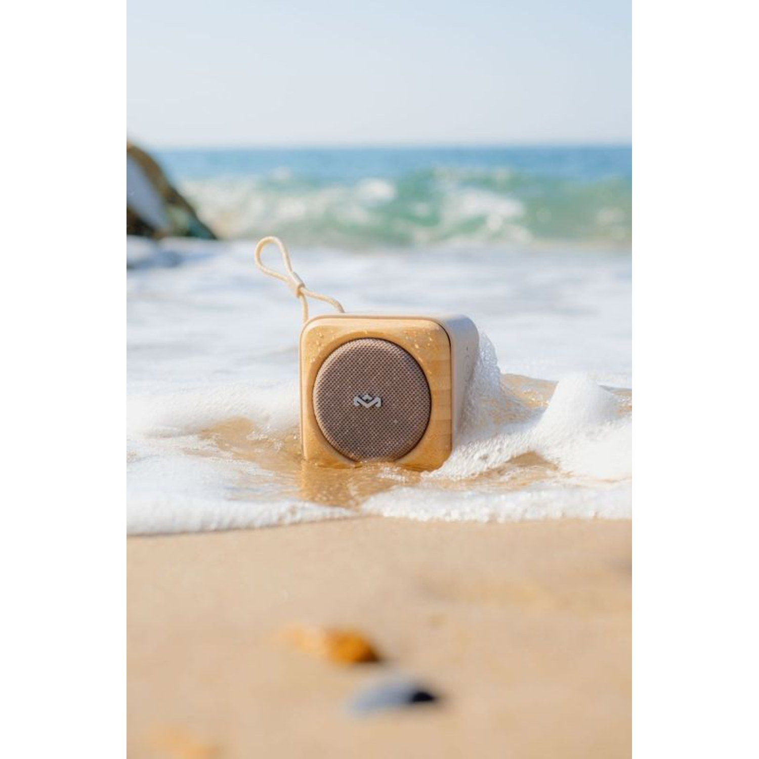 Een houten luidspreker in het water op een strand, met zeegolven en zand.