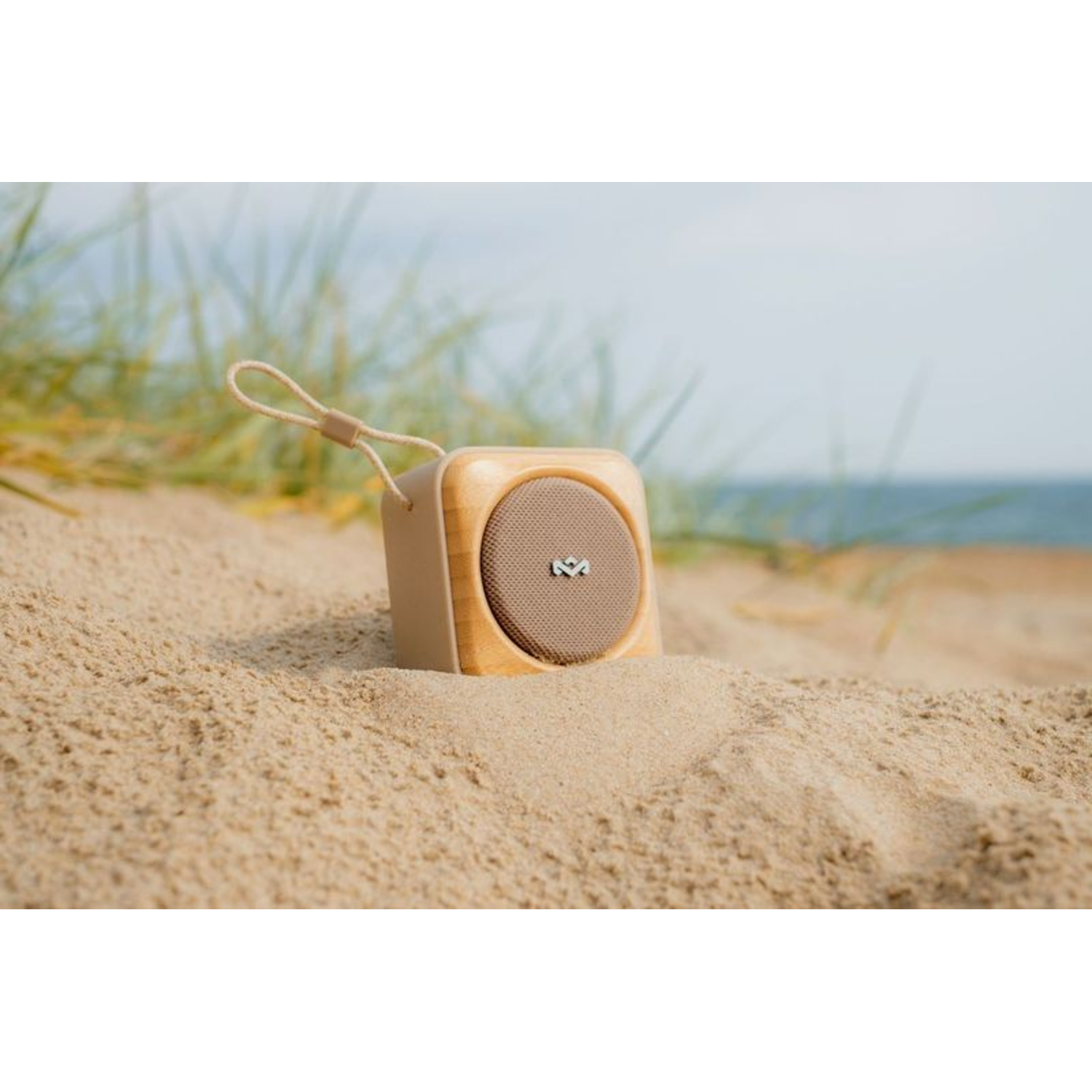 Houten speaker op zand. Beige speaker, bruin gaas. Touw handvat. Achtergrond strand.