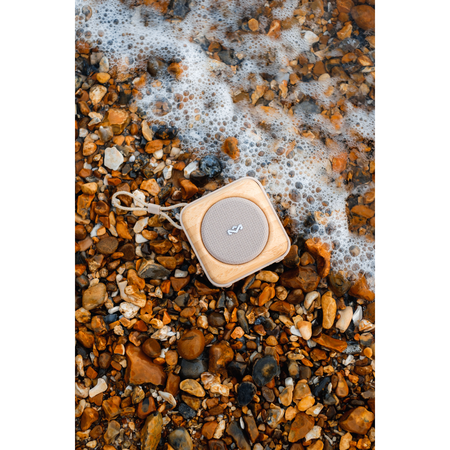 Houten speaker op kiezelstenen op het strand. Wit schuim van de golven. Bovenaanzicht.