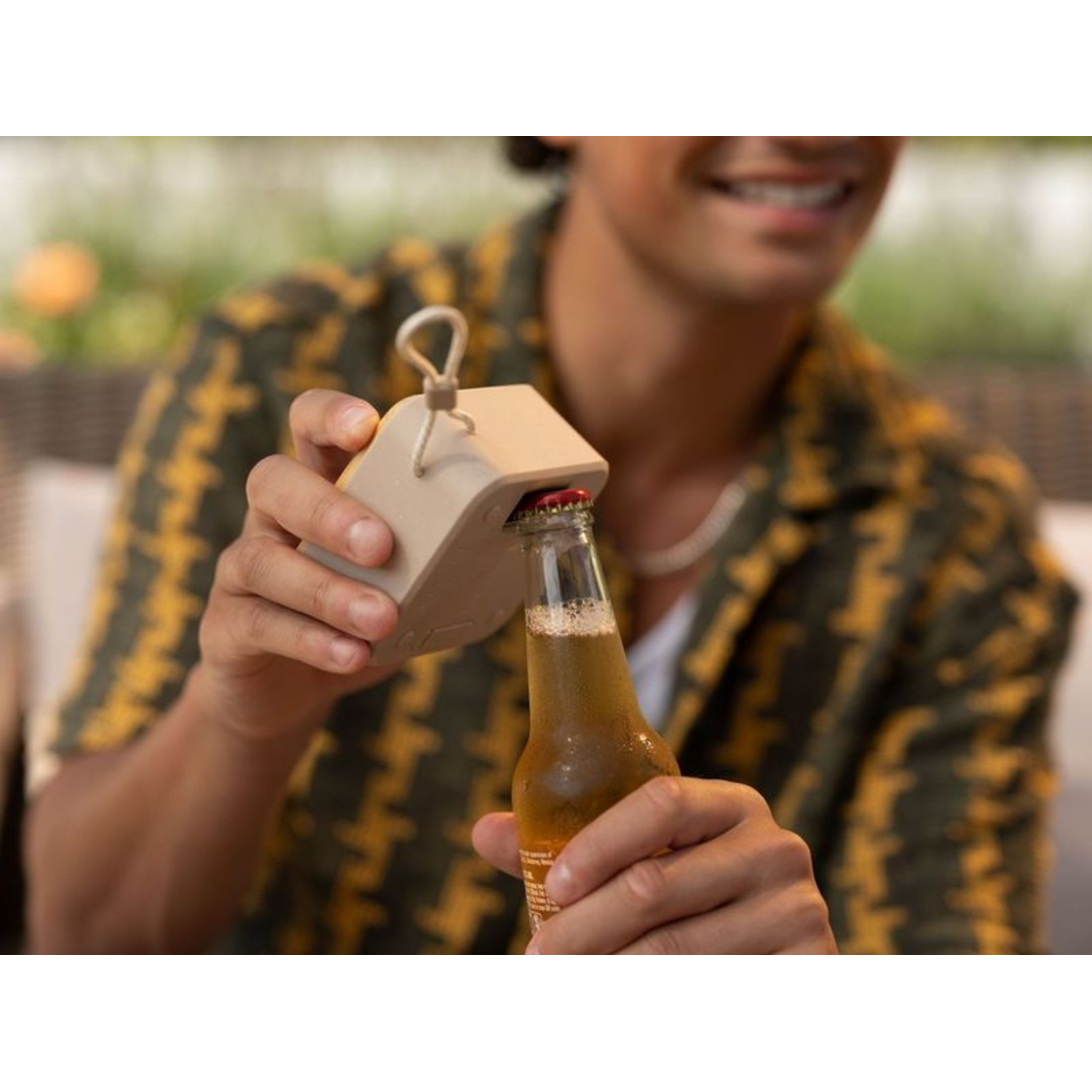 Een man die een bierfles opent met een beige flesopener. Hij draagt ​​een geel overhemd.