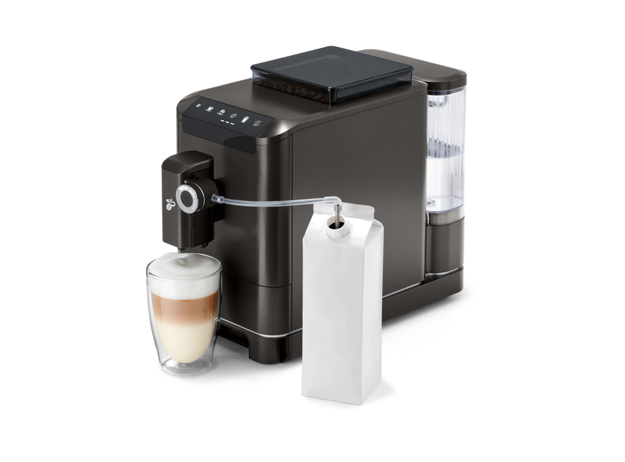 Süt kabı ve bir bardak latte ile bir kahve makinesi. Makine siyah bir yüzey üzerinde.