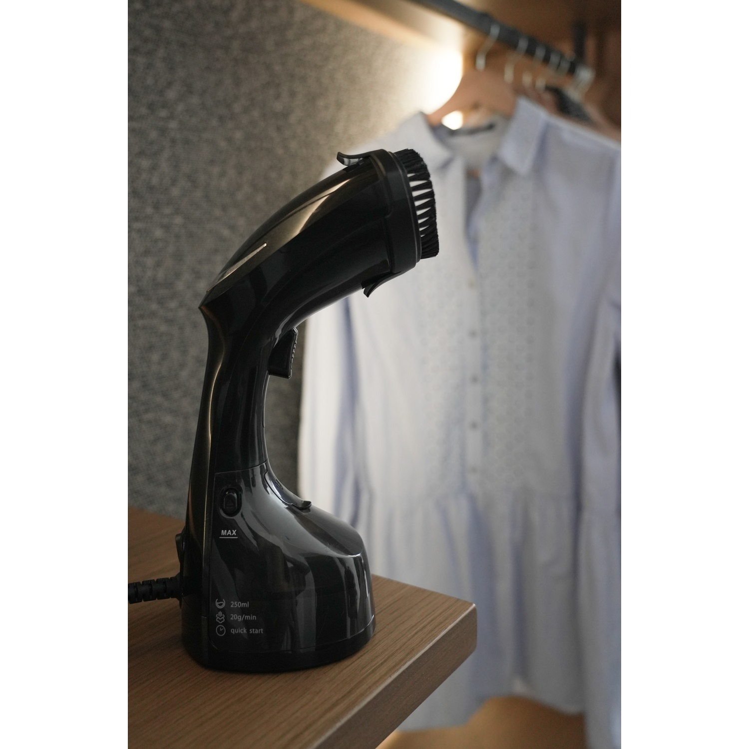 Un vaporizzatore per vestiti nero su un tavolo di legno, con una camicia appesa sullo sfondo sfocato.