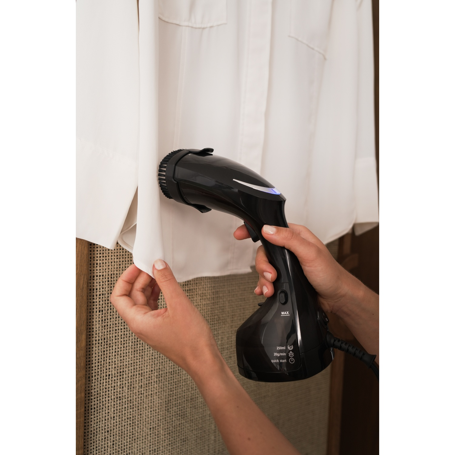 Mani stirano camicia bianca con vaporiera nera, vista ravvicinata.