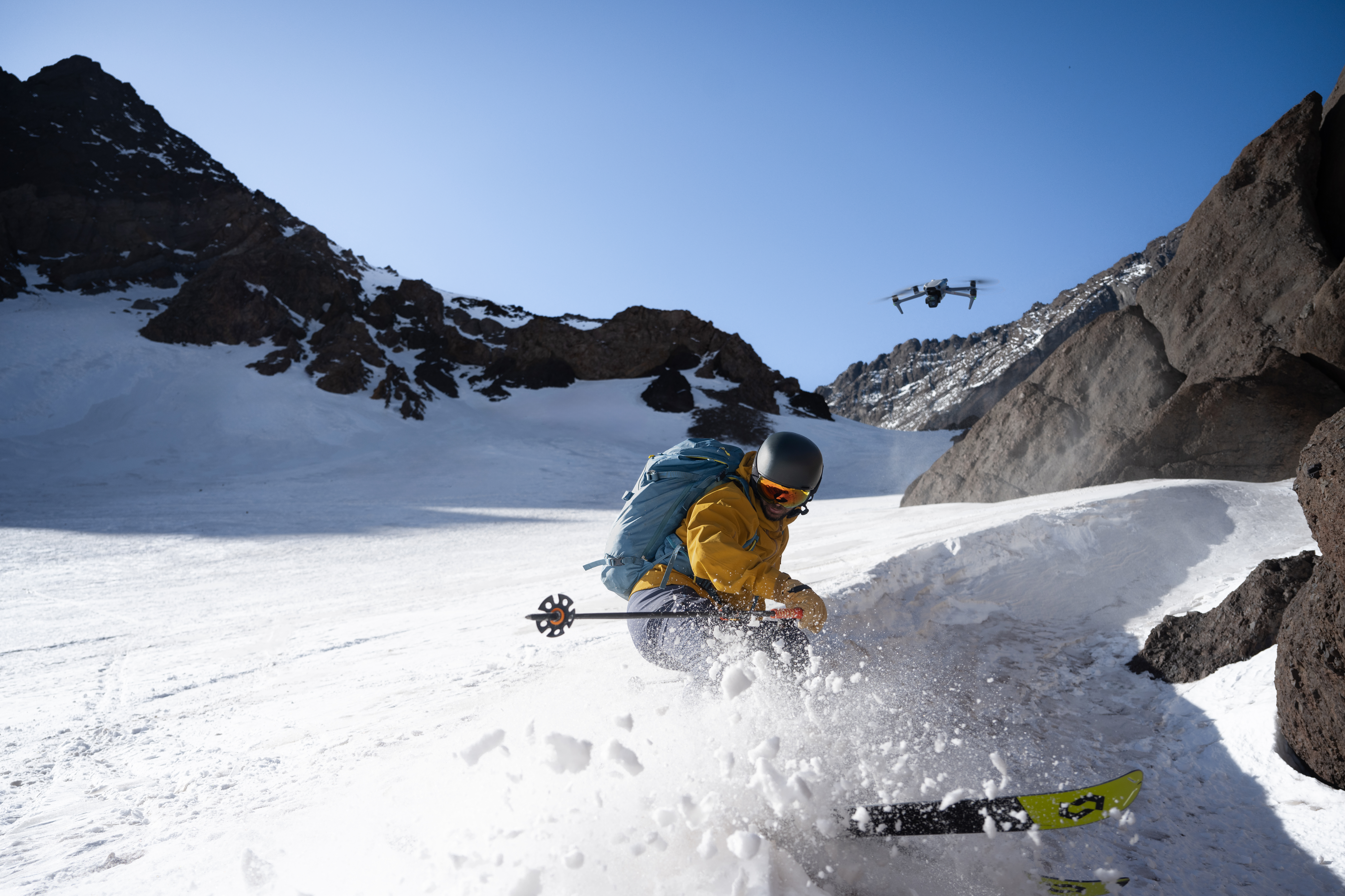 Narciarz zjeżdżający po zaśnieżonym stoku. Dron unosi się na niebie.