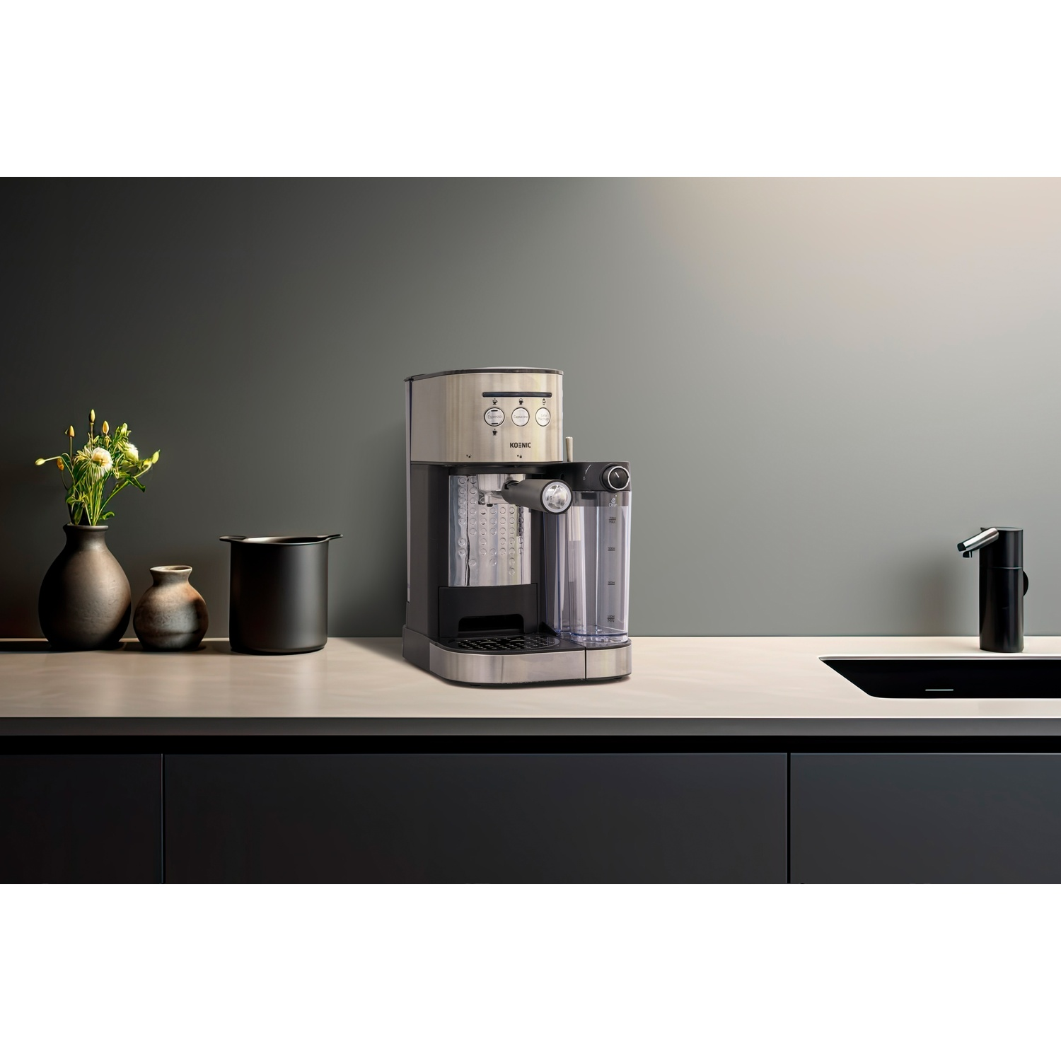 Macchina per caffè espresso sul bancone, con vasi e lavandino nero sullo sfondo.