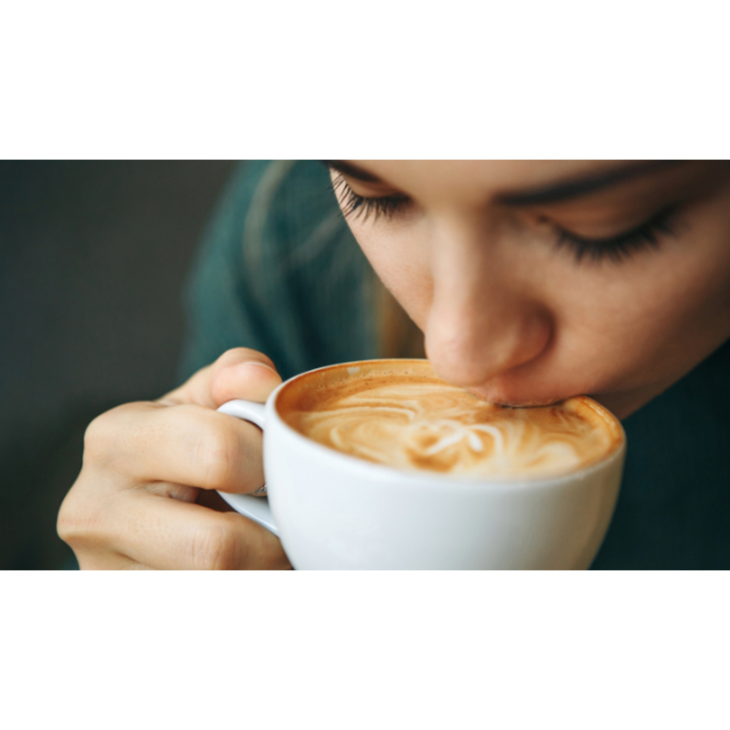 Una donna beve un cappuccino. Si china sulla tazza, con gli occhi chiusi, godendosi la bevanda.