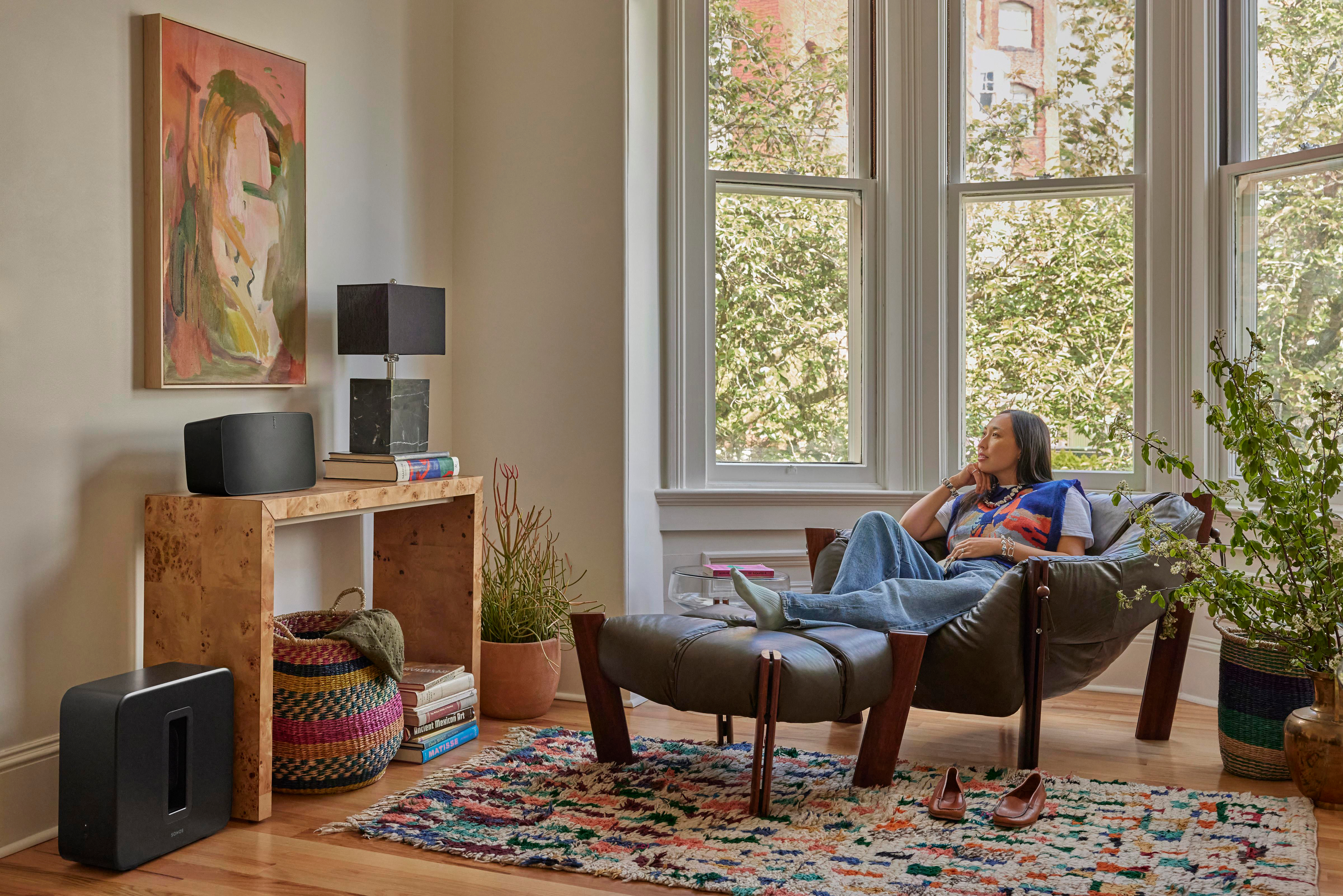 Eine Frau entspannt sich in einem Stuhl in einem Zimmer mit Fenster. Kunst und Bücher sind sichtbar.