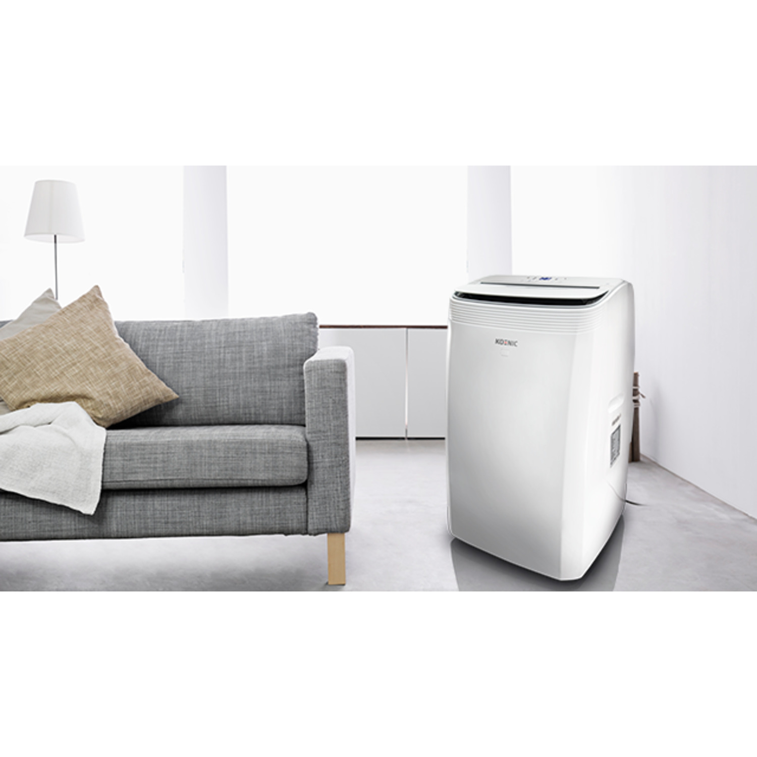 White air conditioner next to a gray couch in a room with a lamp.