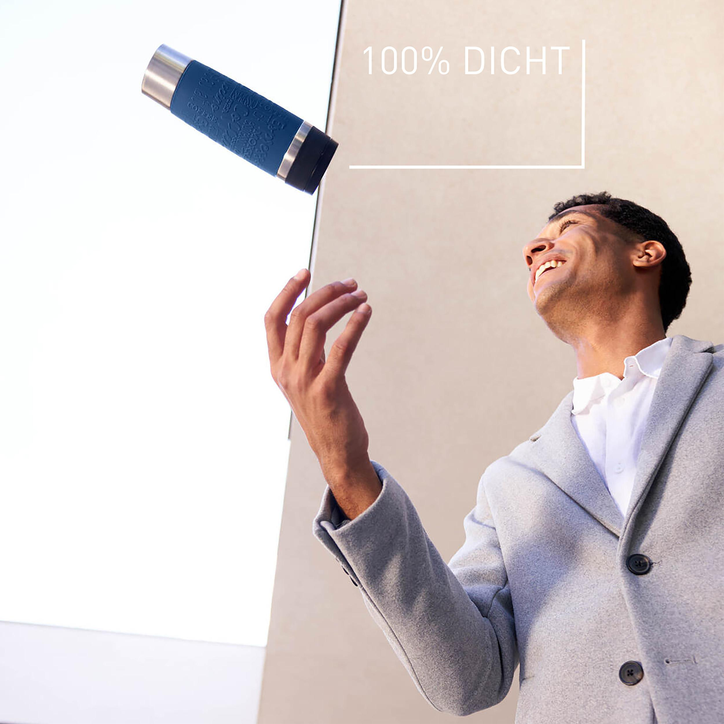 Ein Mann in einem grauen Mantel wirft eine blaue Thermoskanne in die Luft, im Freien.