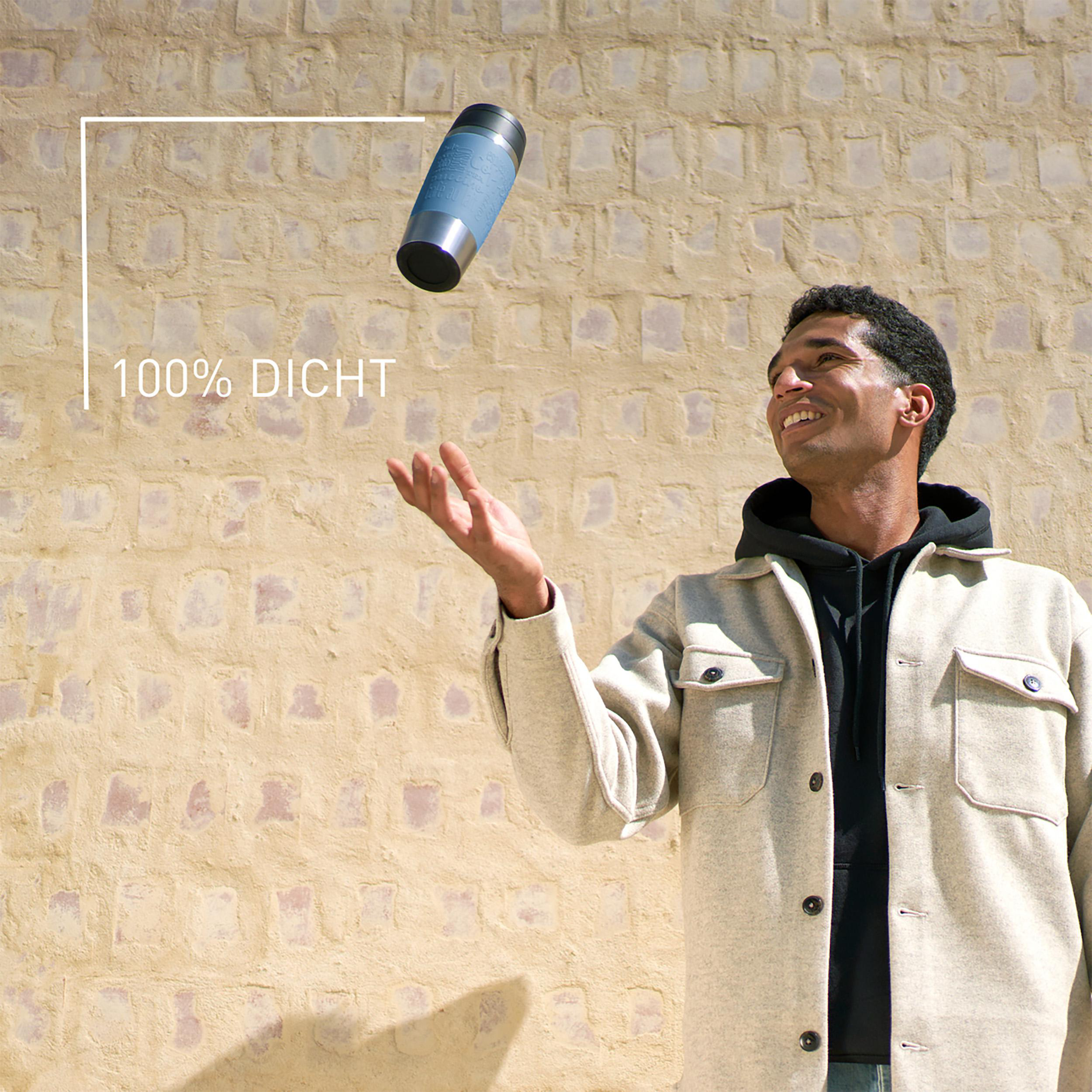 Ein Mann wirft einen blau-silbernen Reisebecher in die Luft. Der Hintergrund ist eine strukturierte beige Wand.