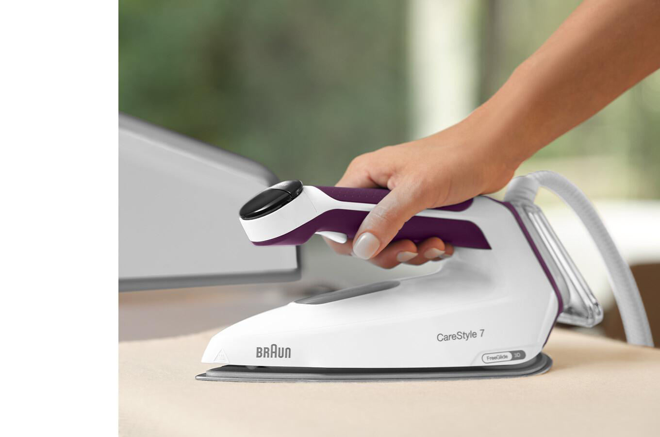 Weißes und lila Bügeleisen. Eine Hand hält den Griff. Heller Hintergrund. Braun CareStyle 7 steht drauf.
