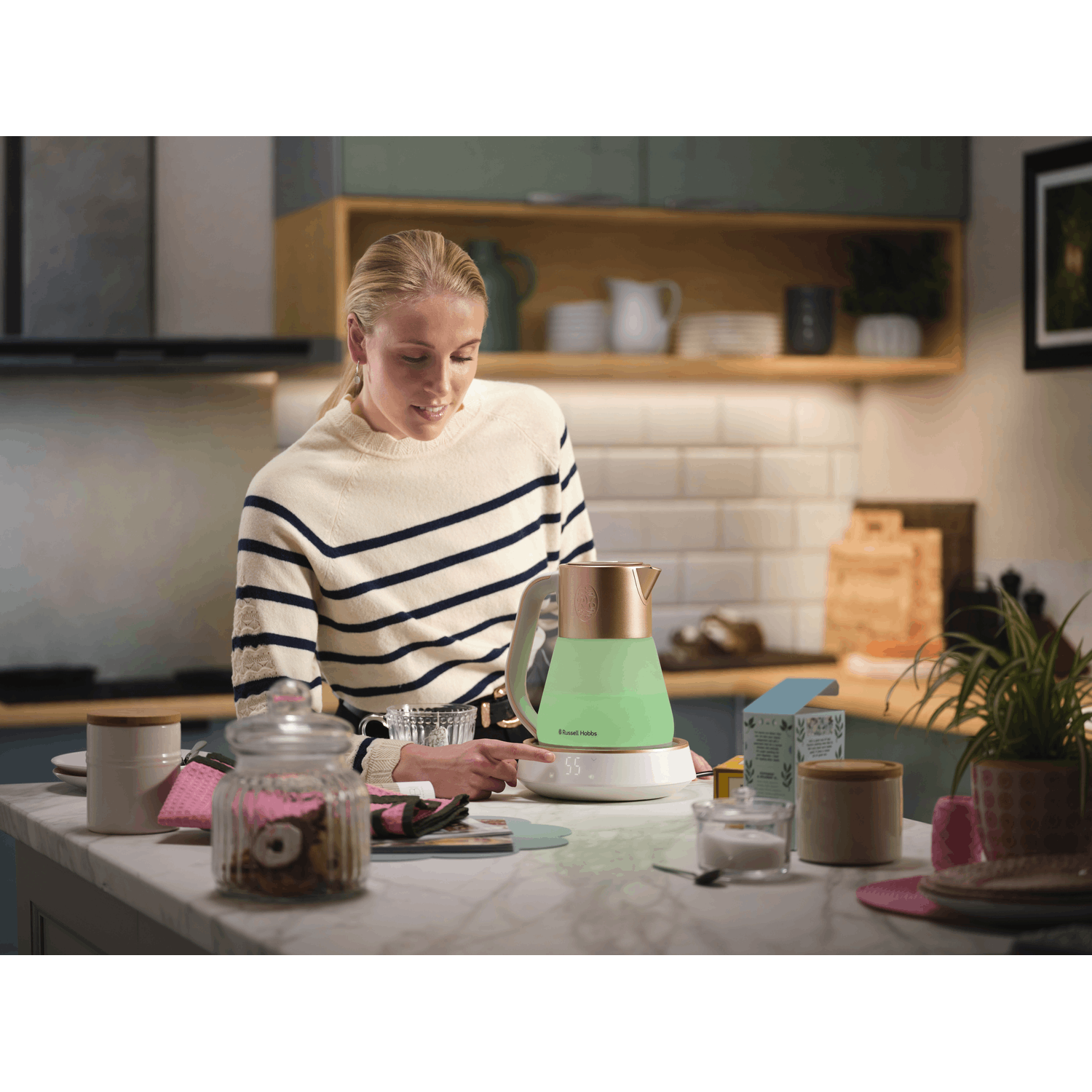 Woman in kitchen using a kettle with a digital display, other items on counter.
