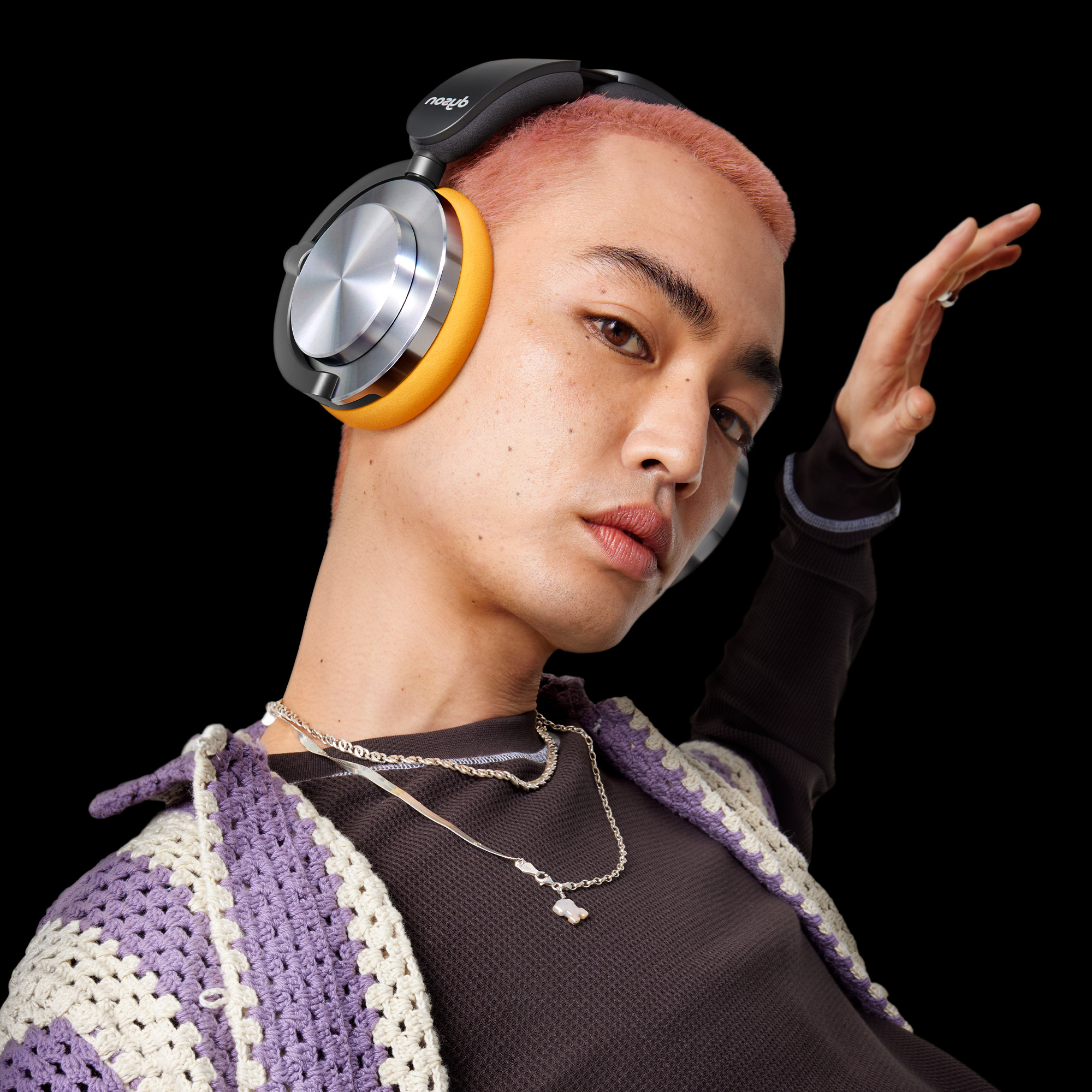 Mężczyzna z różowymi włosami, słuchawkami i podniesioną ręką. Czarne tło.