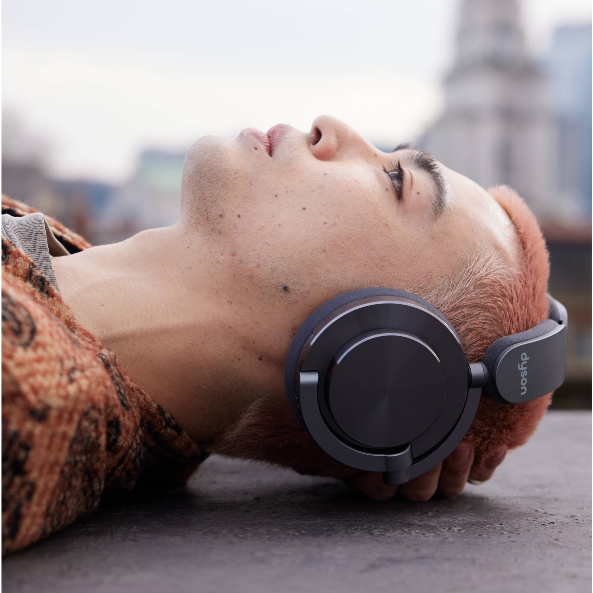 Mężczyzna z różowymi włosami w słuchawkach leżący na powierzchni, patrzący w górę.