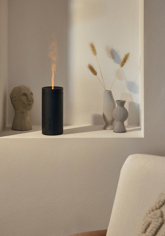 Czarny dyfuzor emitujący parę w kształcie płomienia, z dekoracjami na białej półce.