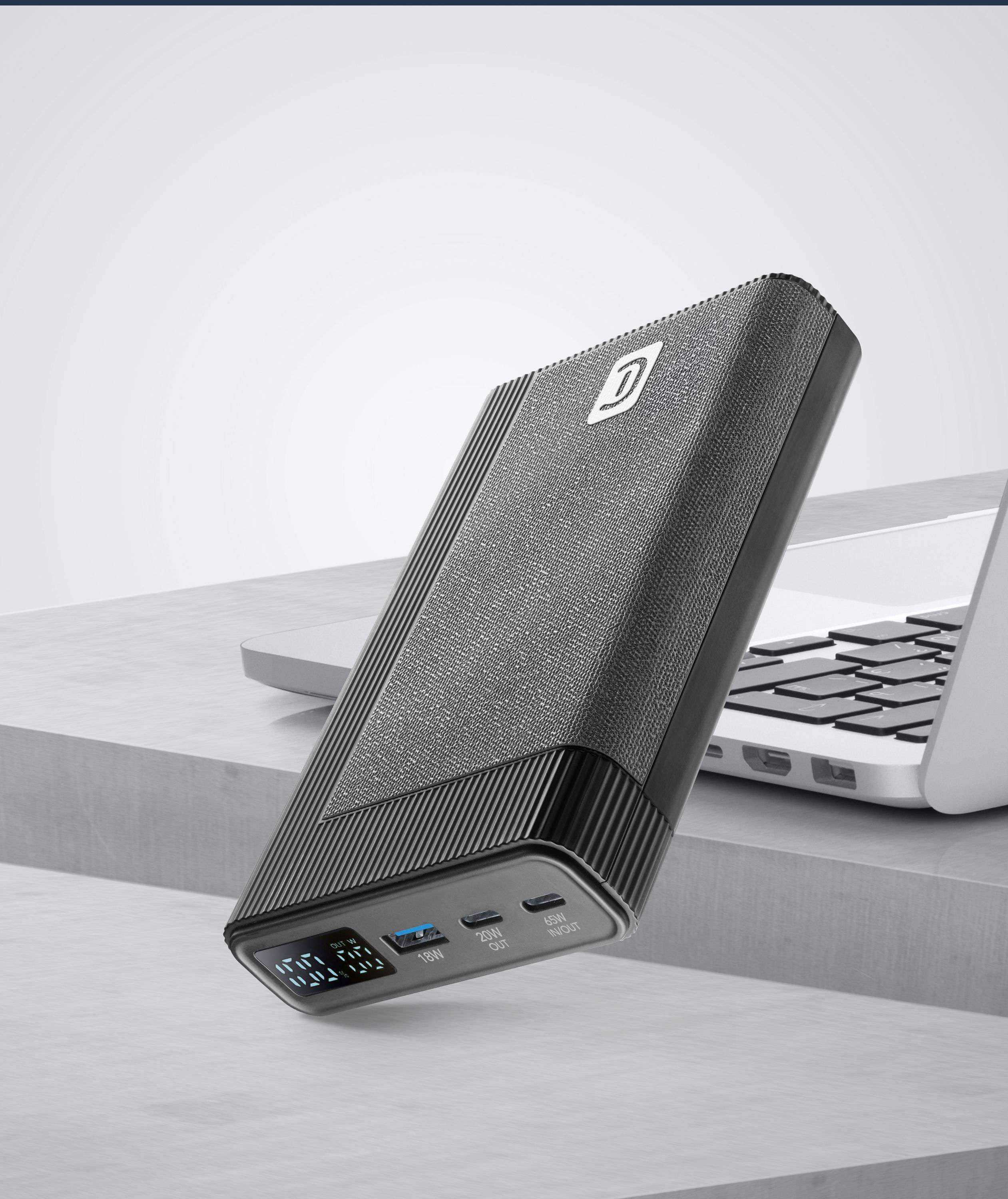 Siyah ve gri powerbank bir masada. Arka planda bir dizüstü bilgisayar var.