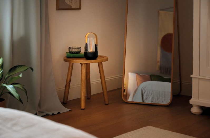 Lampion na drewnianym stoliku, lustro, łóżko i zasłony, tworzące przytulną scenę.