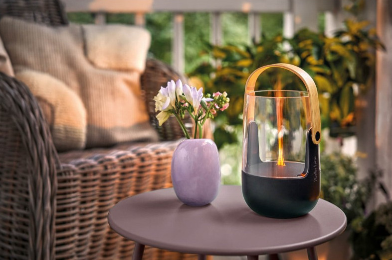 Lampa i wazon z kwiatami na stole obok wiklinowego krzesła na werandzie.