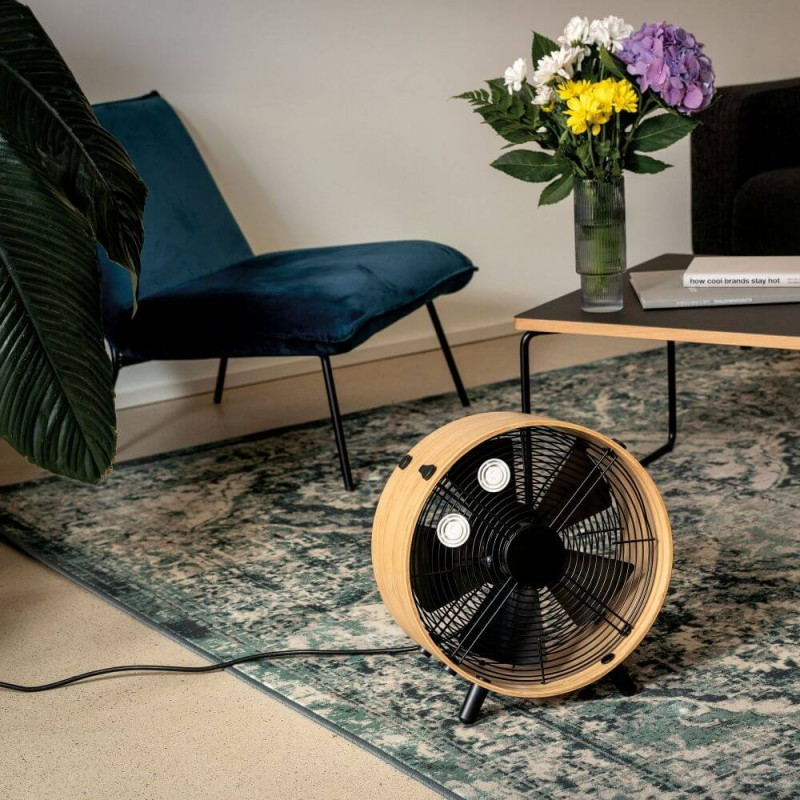 Drewniany wentylator na wzorzystym dywanie, kwiaty w wazonie, krzesło i stół.