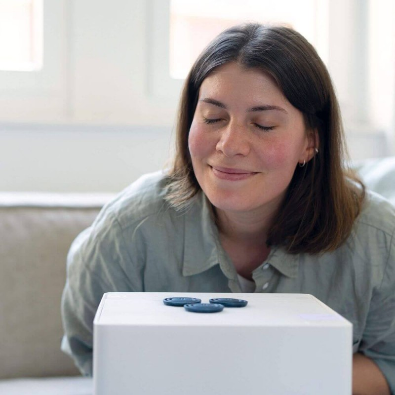 Kobieta uśmiecha się, patrząc na trzy niebieskie dyski na białej powierzchni. Tłem jest pokój.