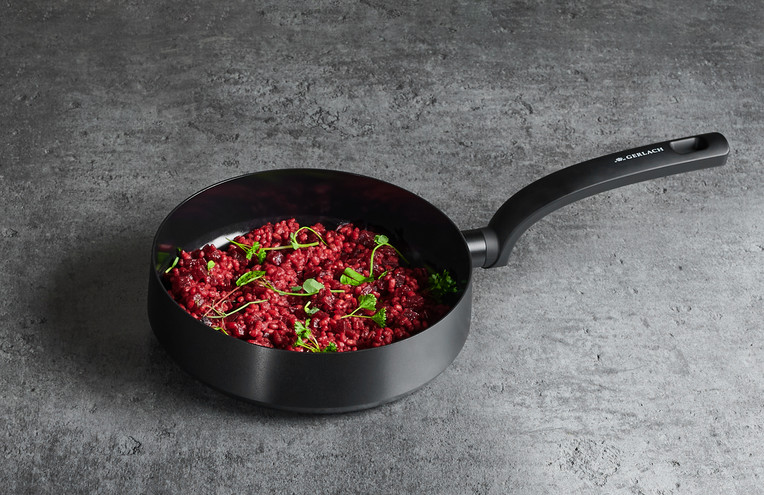 Czarny patelnia z risotto. Risotto czerwone, z zielonymi ziołami. Czarny uchwyt.