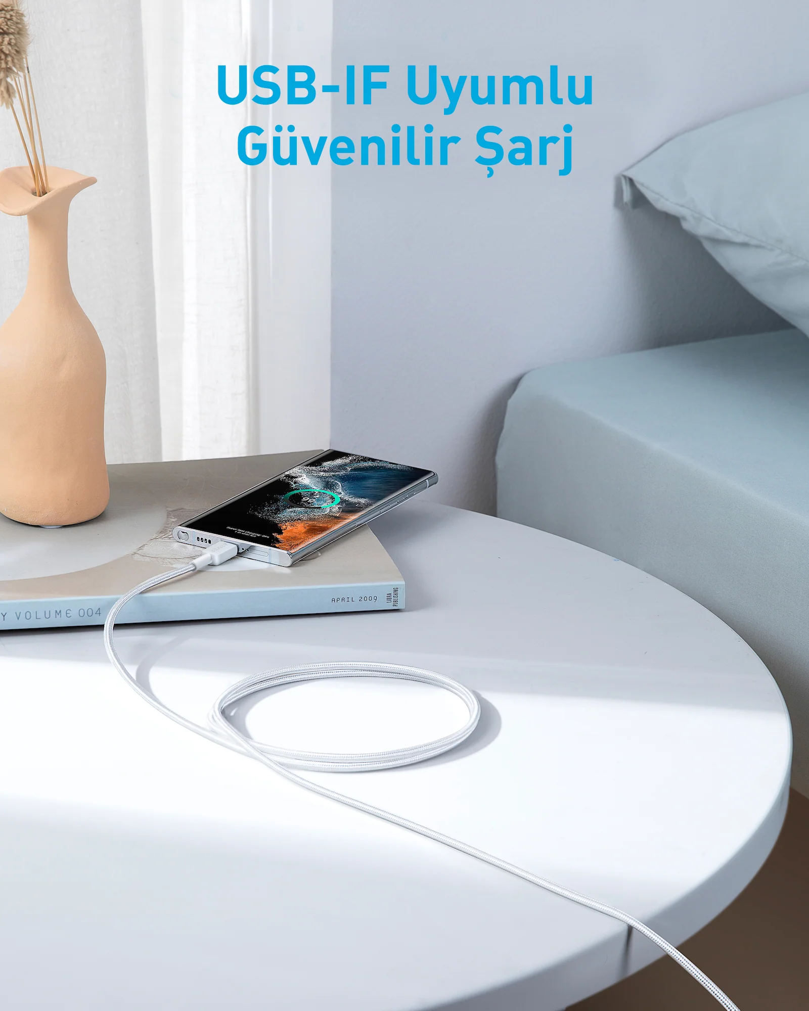Bir vazoyla, arka planda yatakla bir masada bir telefonu şarj eden beyaz bir kablo.
