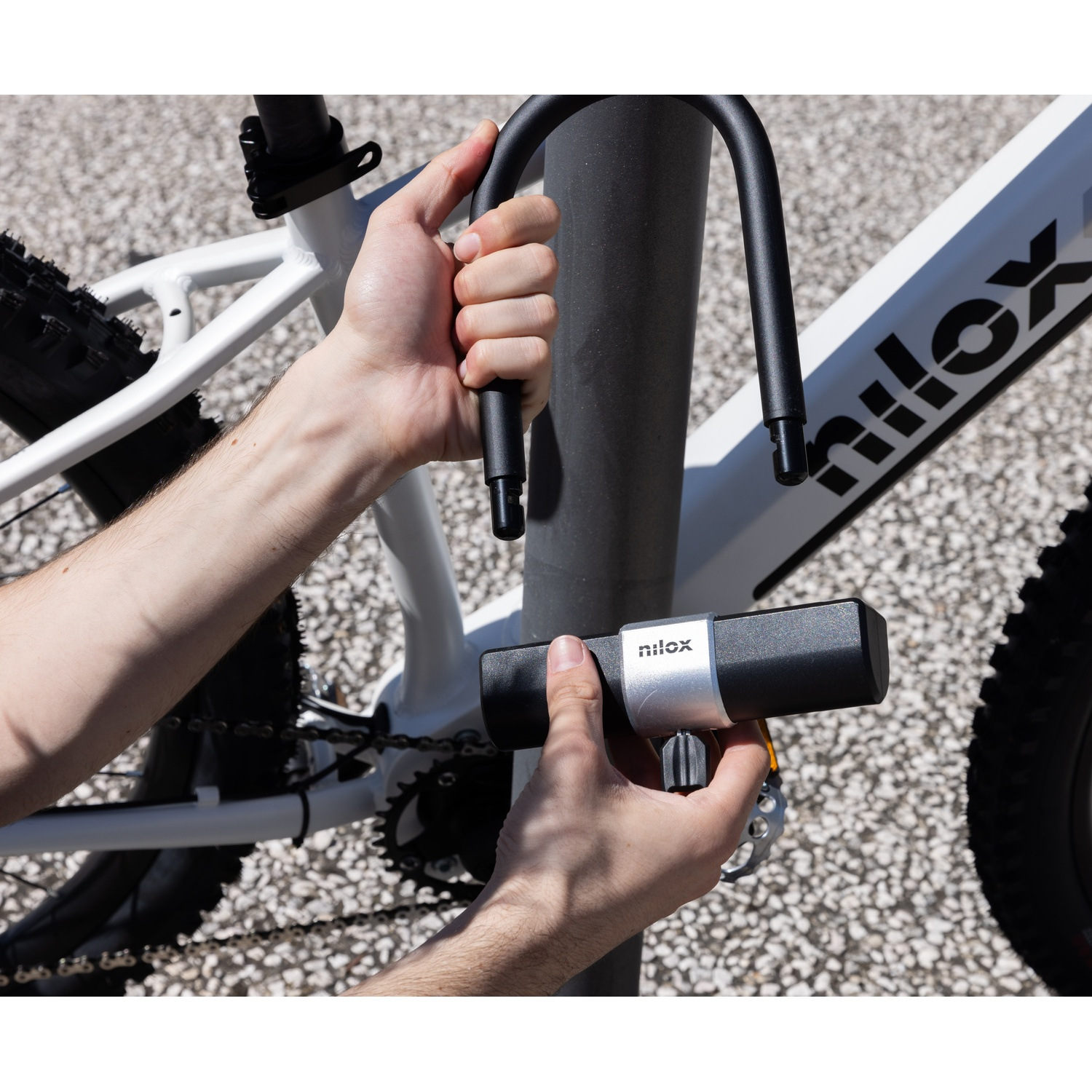 Mani che bloccano un lucchetto a forma di U su una bicicletta vicino a un palo.