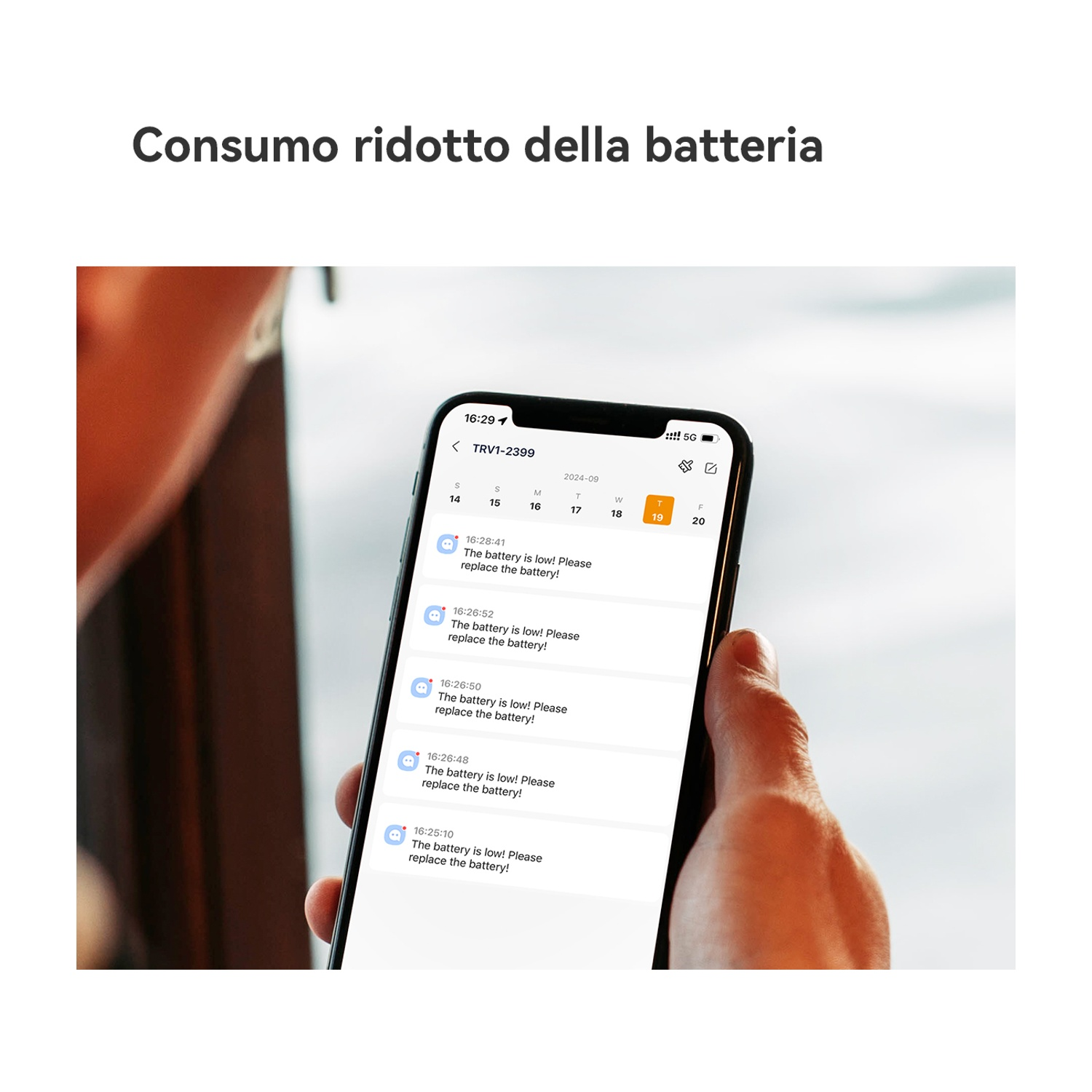 Una mano tiene un telefono che mostra un avviso di batteria scarica. Lo sfondo è sfocato.