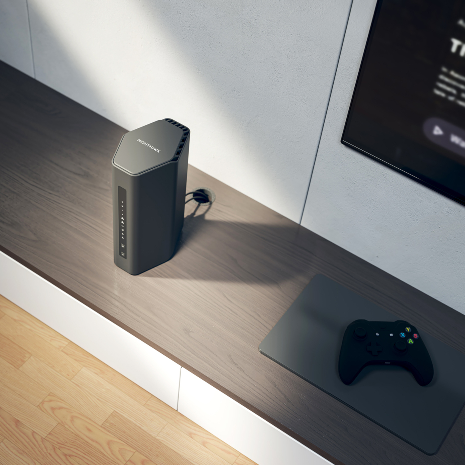 Een zwarte Nighthawk-router op een houten plank naast een tv en een zwarte gamecontroller.