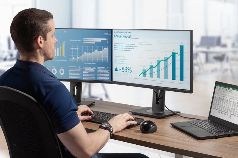 Egy férfi asztalnál dolgozik két monitorral és egy laptopal.