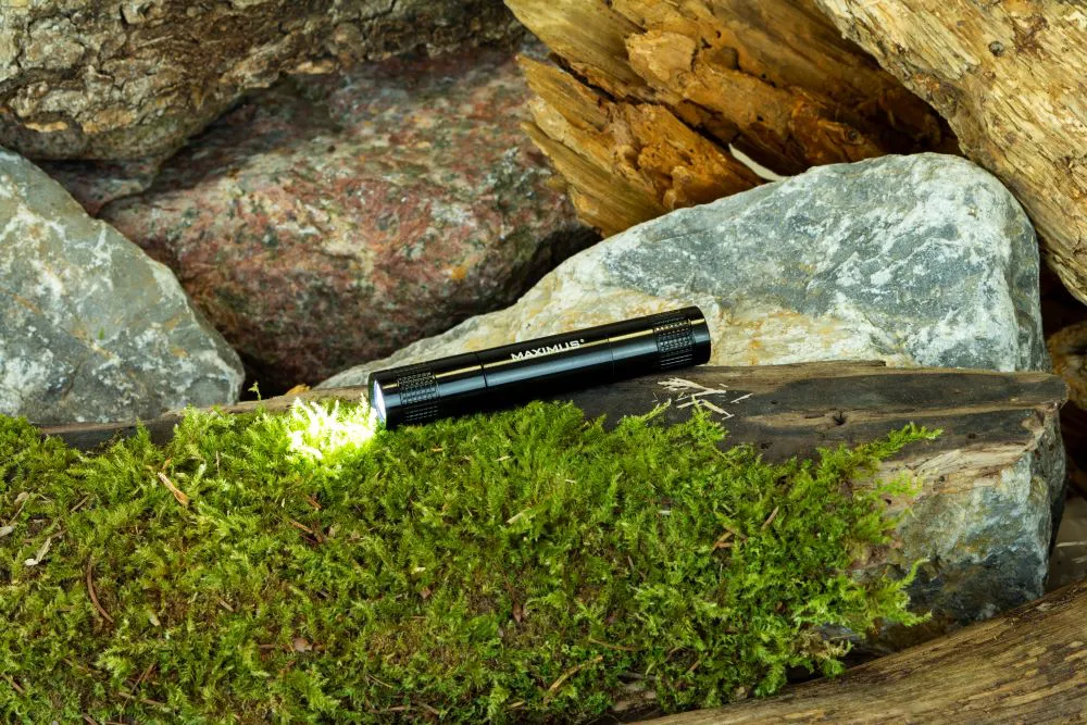 Lampe de poche noire sur une bûche moussue avec des rochers en arrière-plan.