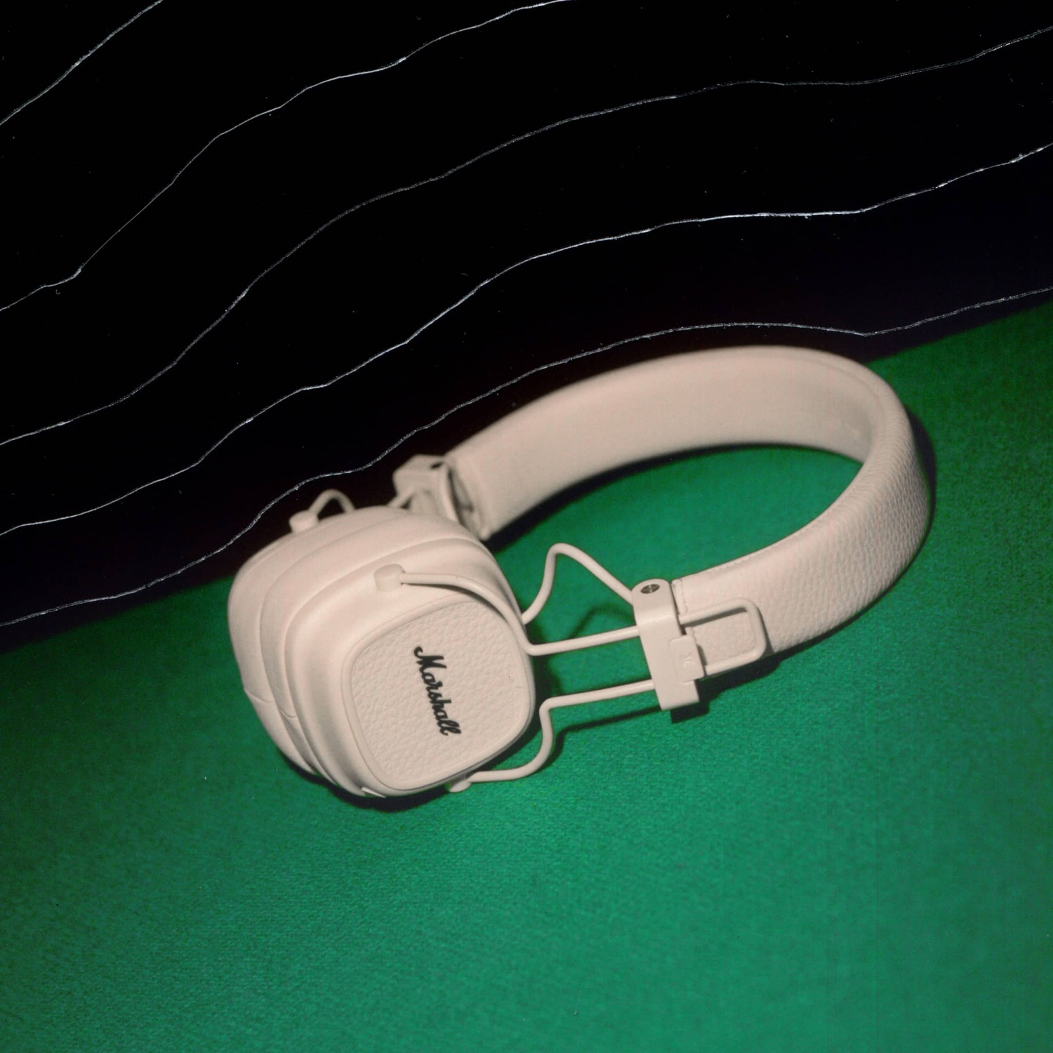 White Marshall headphones on a green surface with a black background and white lines.