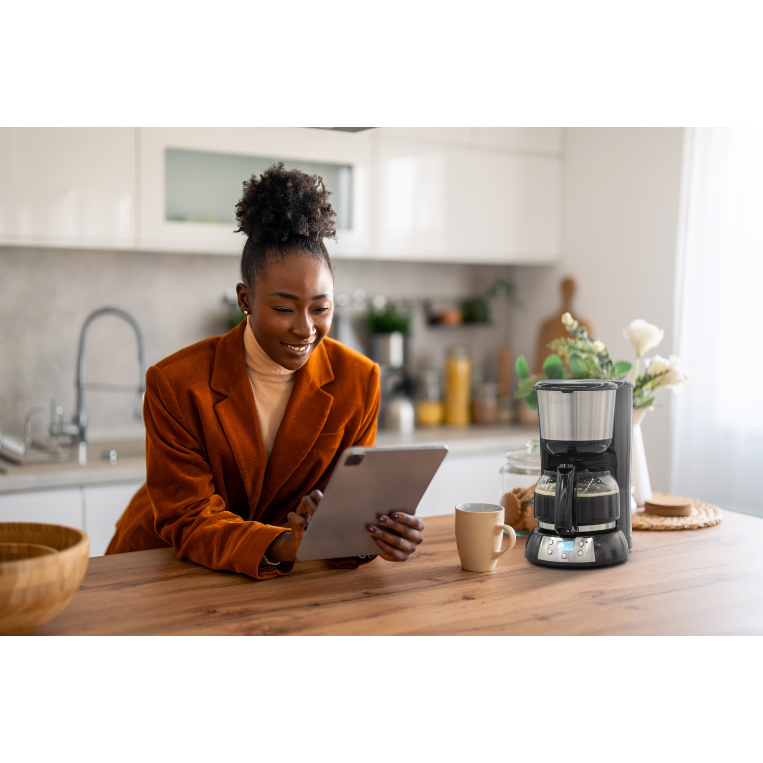 Femme utilisant une tablette dans une cuisine avec cafetière et tasse.
