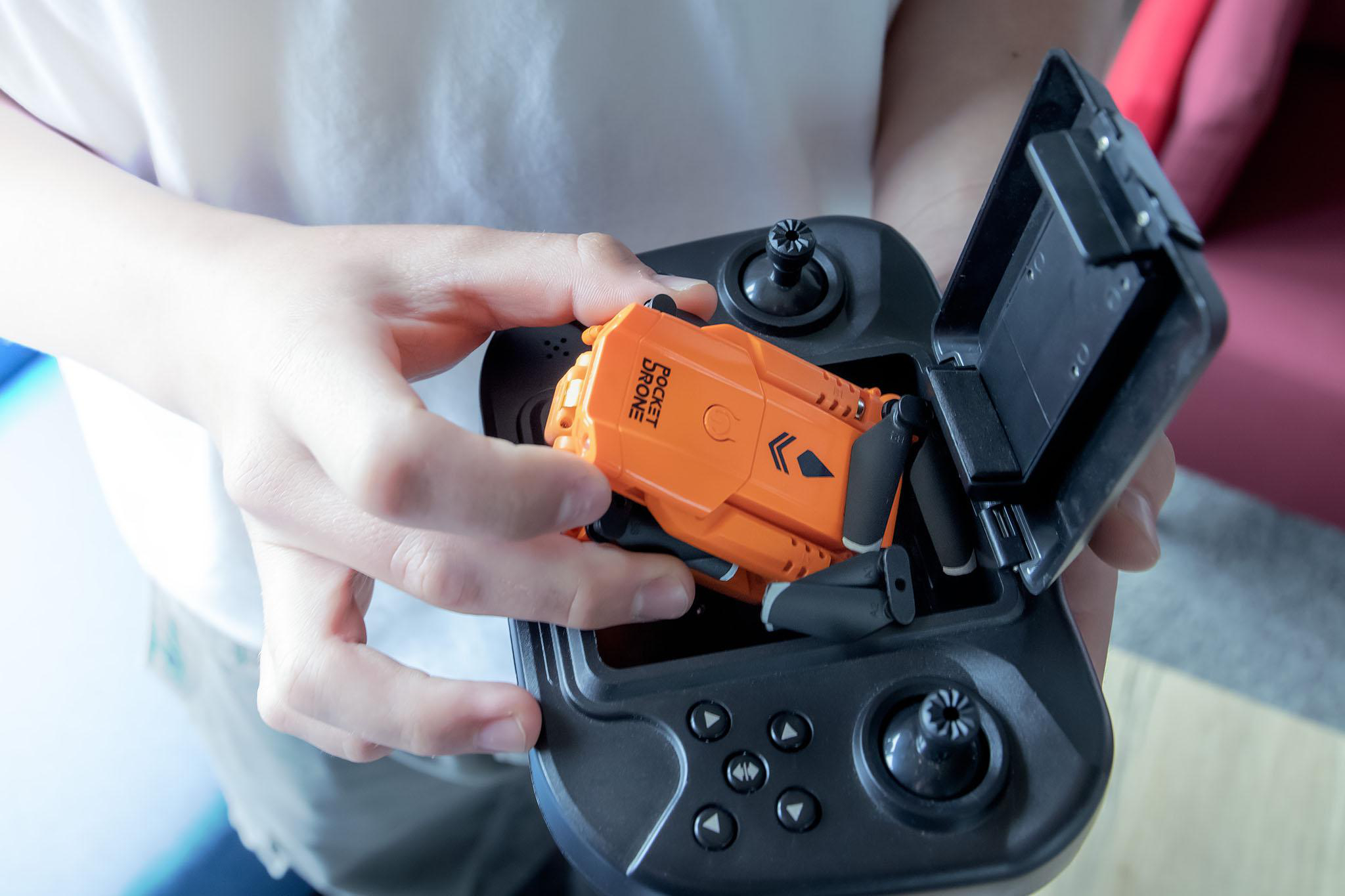 Hände halten eine kleine orangefarbene Drohne in einer Fernbedienung.