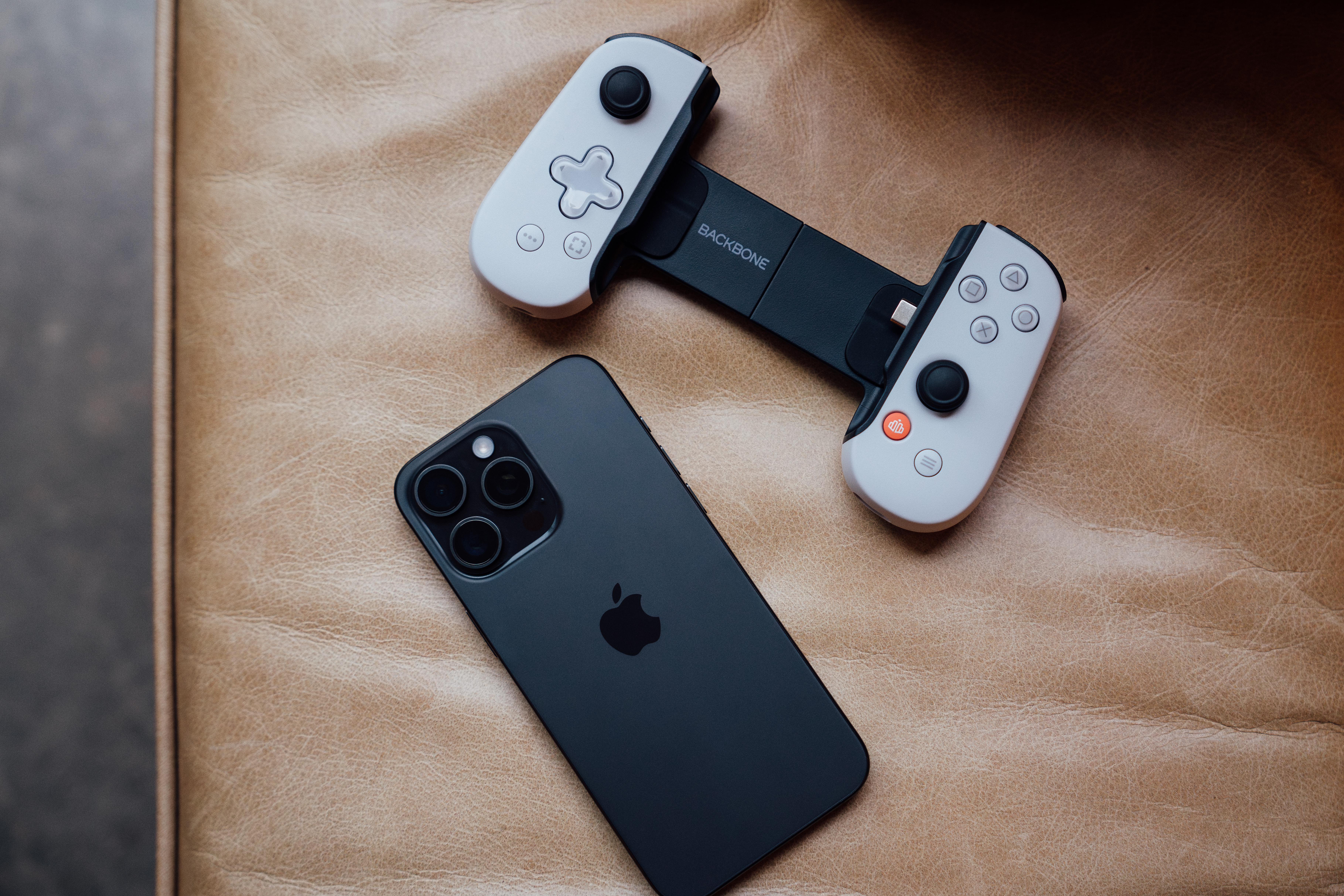 Ein iPhone und ein schwarzer Backbone-Controller liegen auf einer braunen Lederoberfläche. Der Controller ist geöffnet.